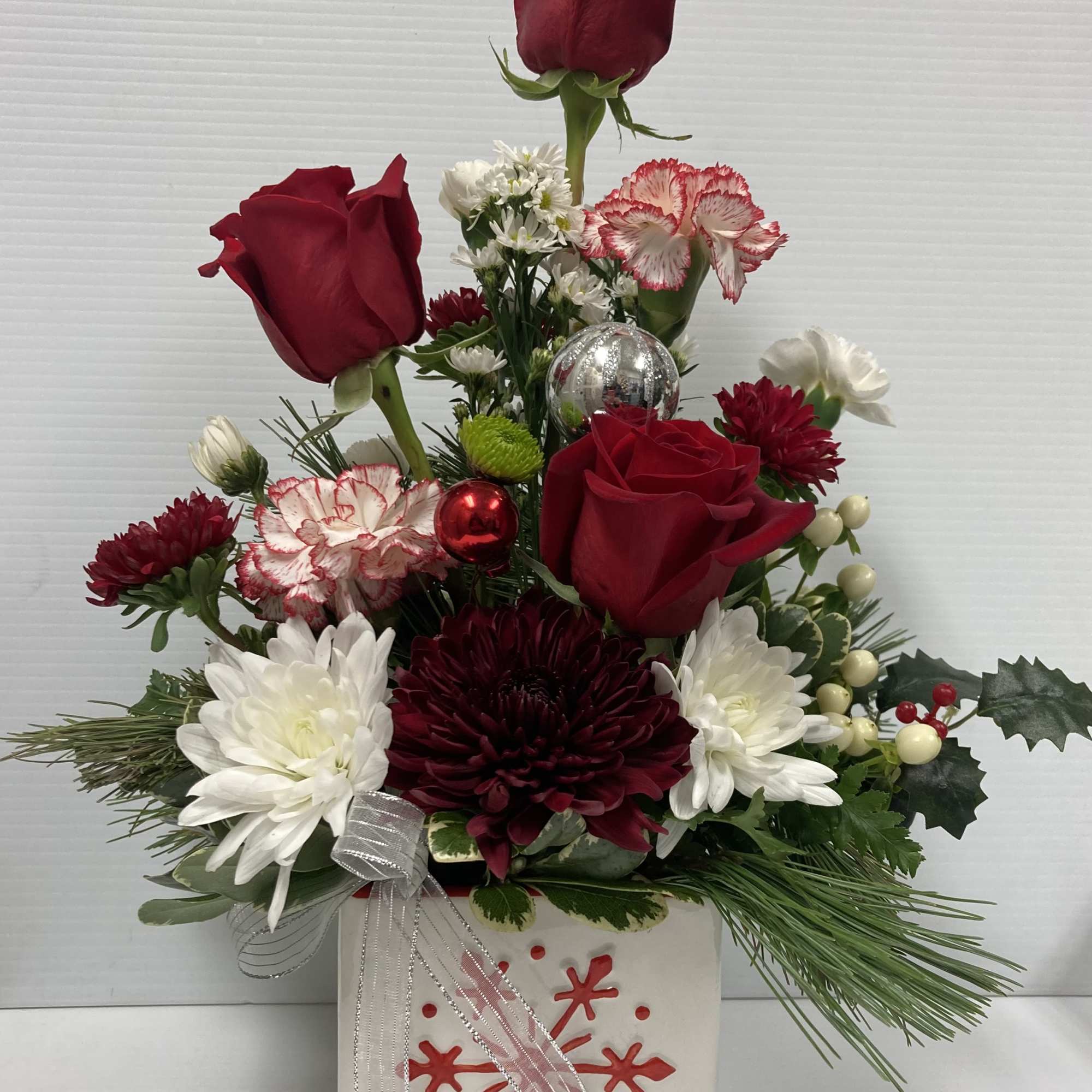 Holiday arrangement in a cute snow flake glass container. Arrangement includes roses