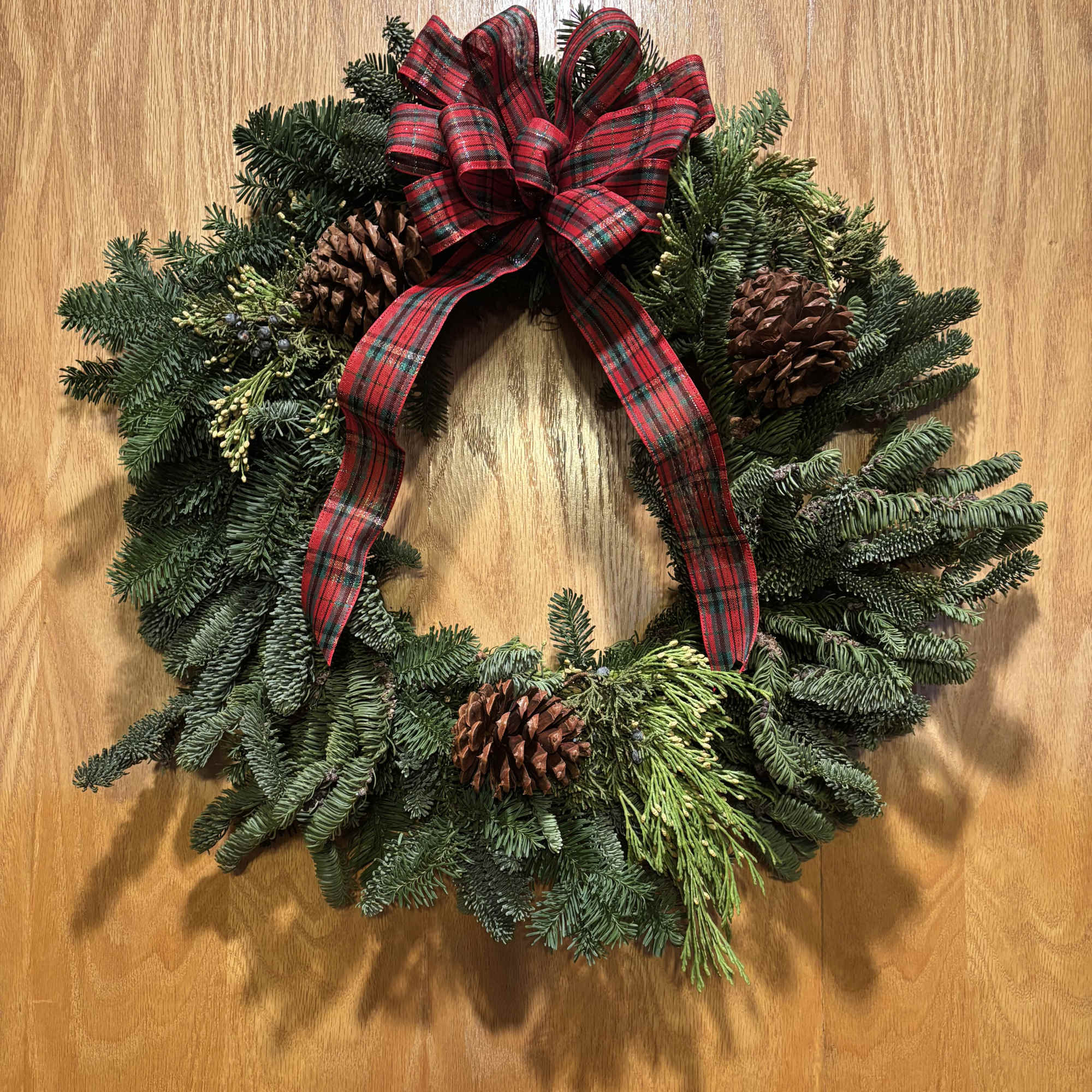 Beautiful live holiday wreath decorated with berries, pine cones, and ribbon. Available