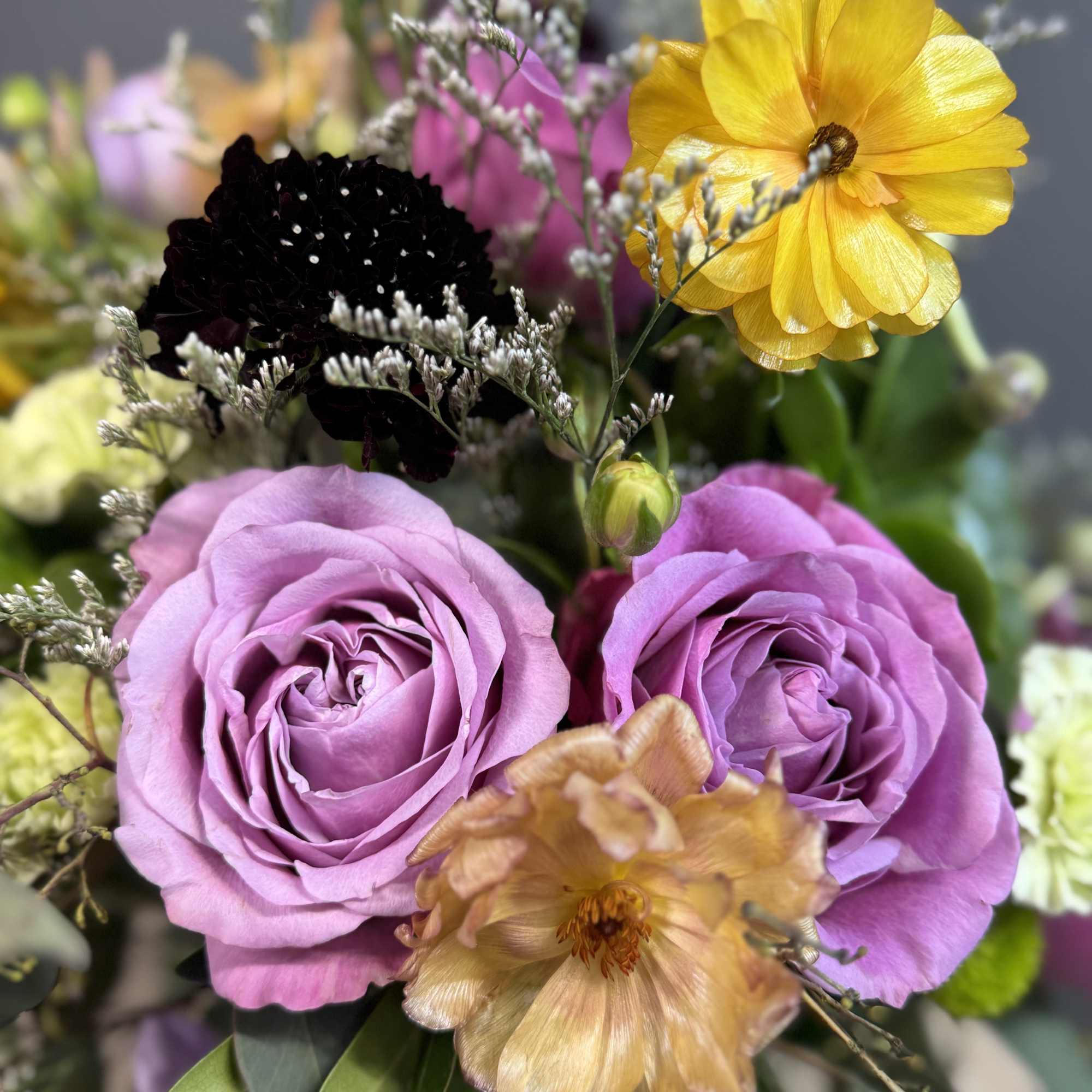 A vibrant medley of lavender roses, golden blooms, and fresh greenery arranged