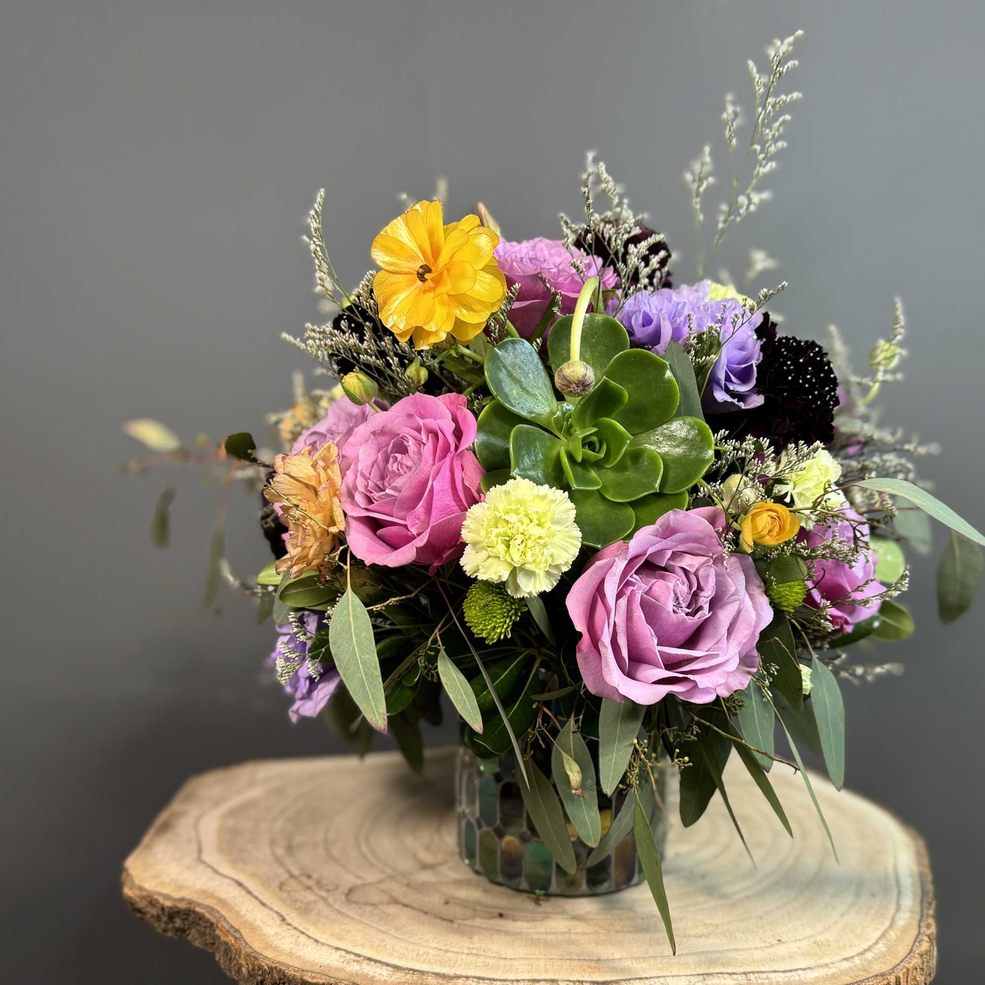 A vibrant medley of lavender roses, golden blooms, and fresh greenery arranged