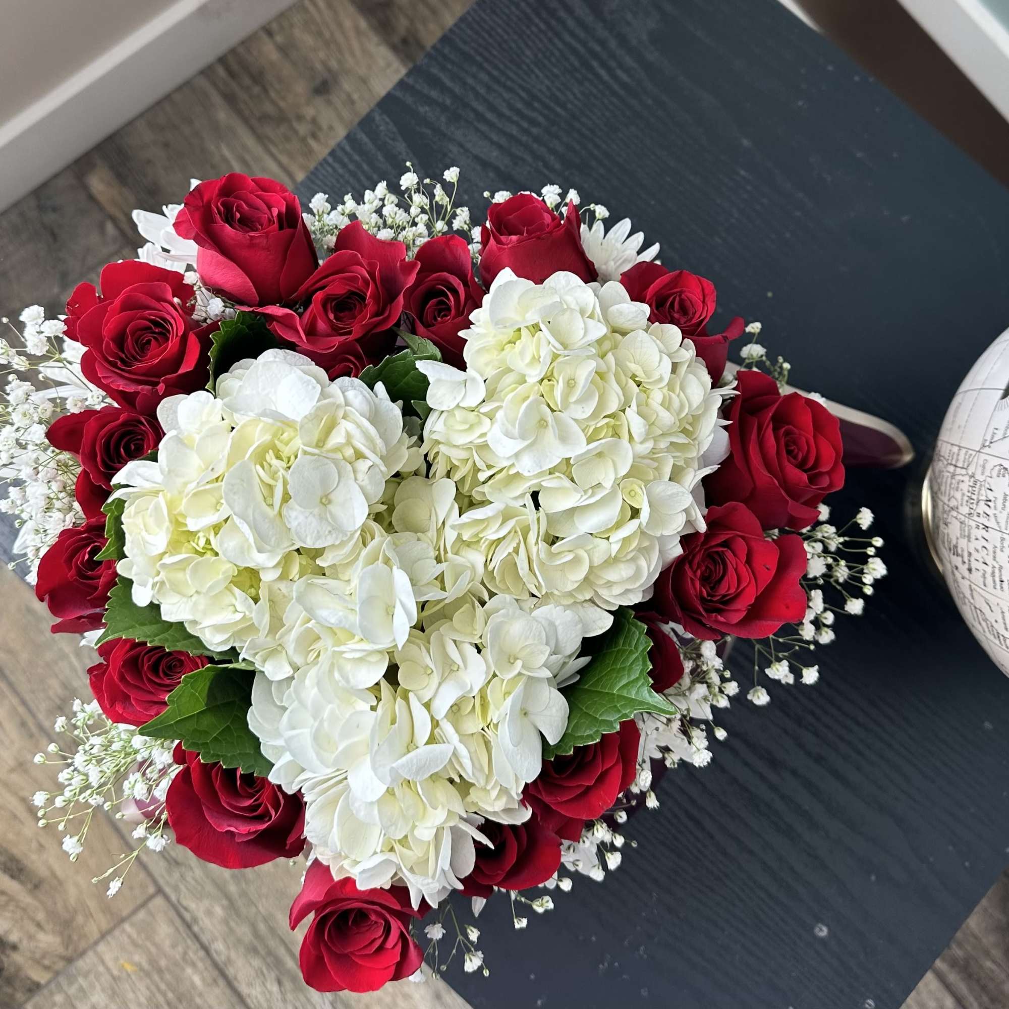 This enchanting arrangement, nestled in a heart-shaped box, features lush white hydrangeas