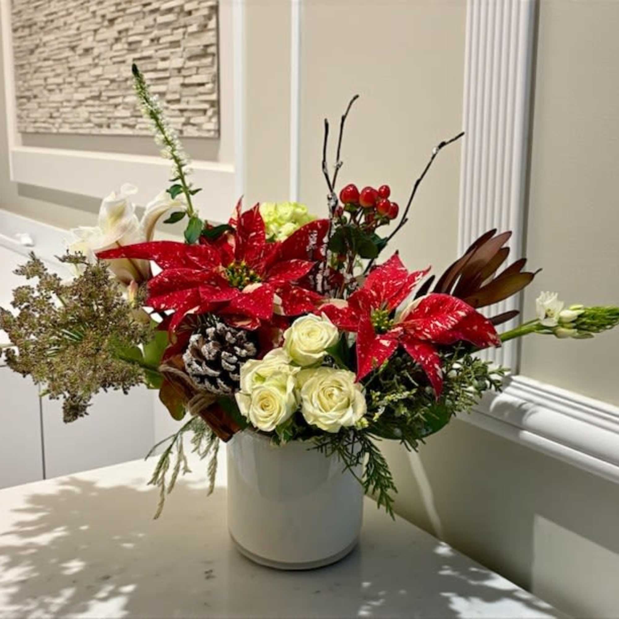 A modern white cylinder filled with rich poinsettias, seasonal blooms, winter pine