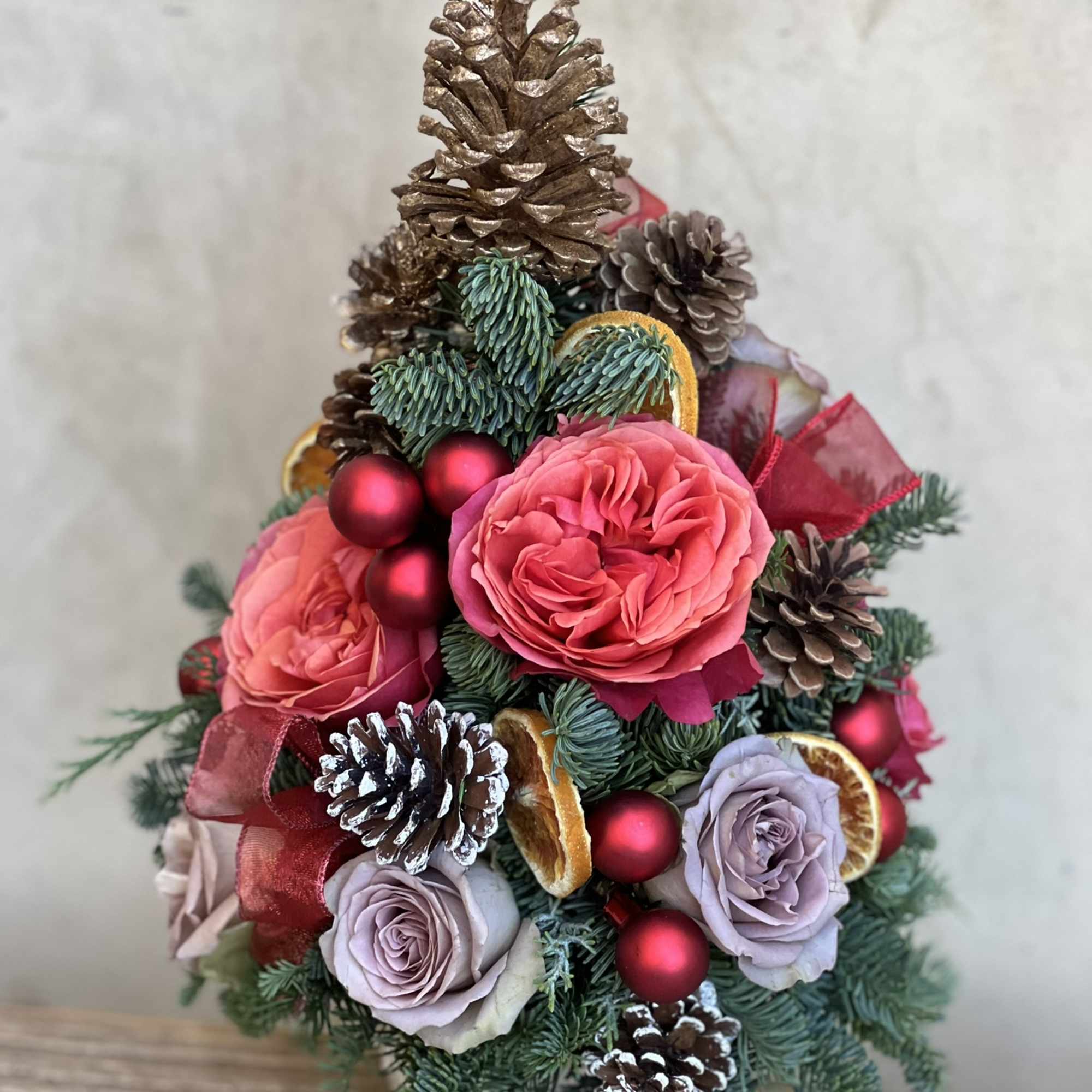 Fresh tabletop Christmas foliage adorned in real roses, pinecones, ribbon and baubles.