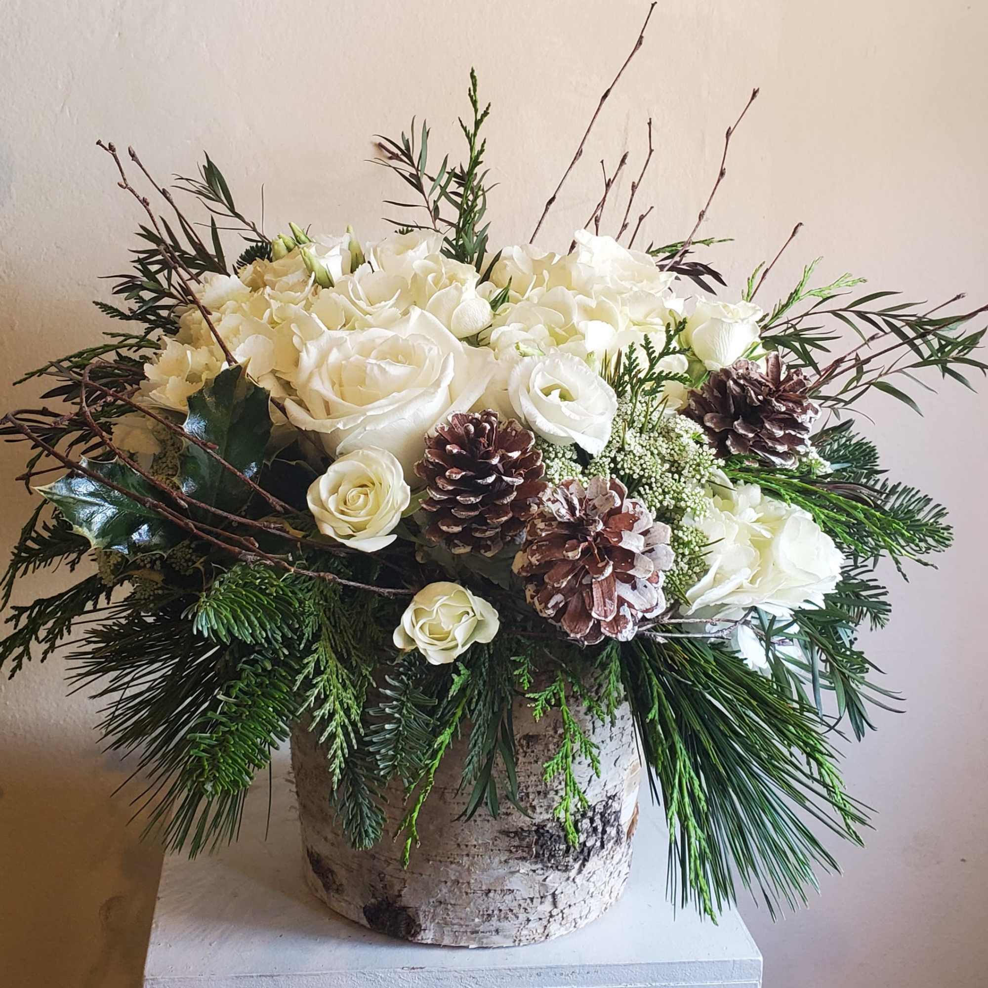 Seasonal white flowers in a birch container with festive pine cones (