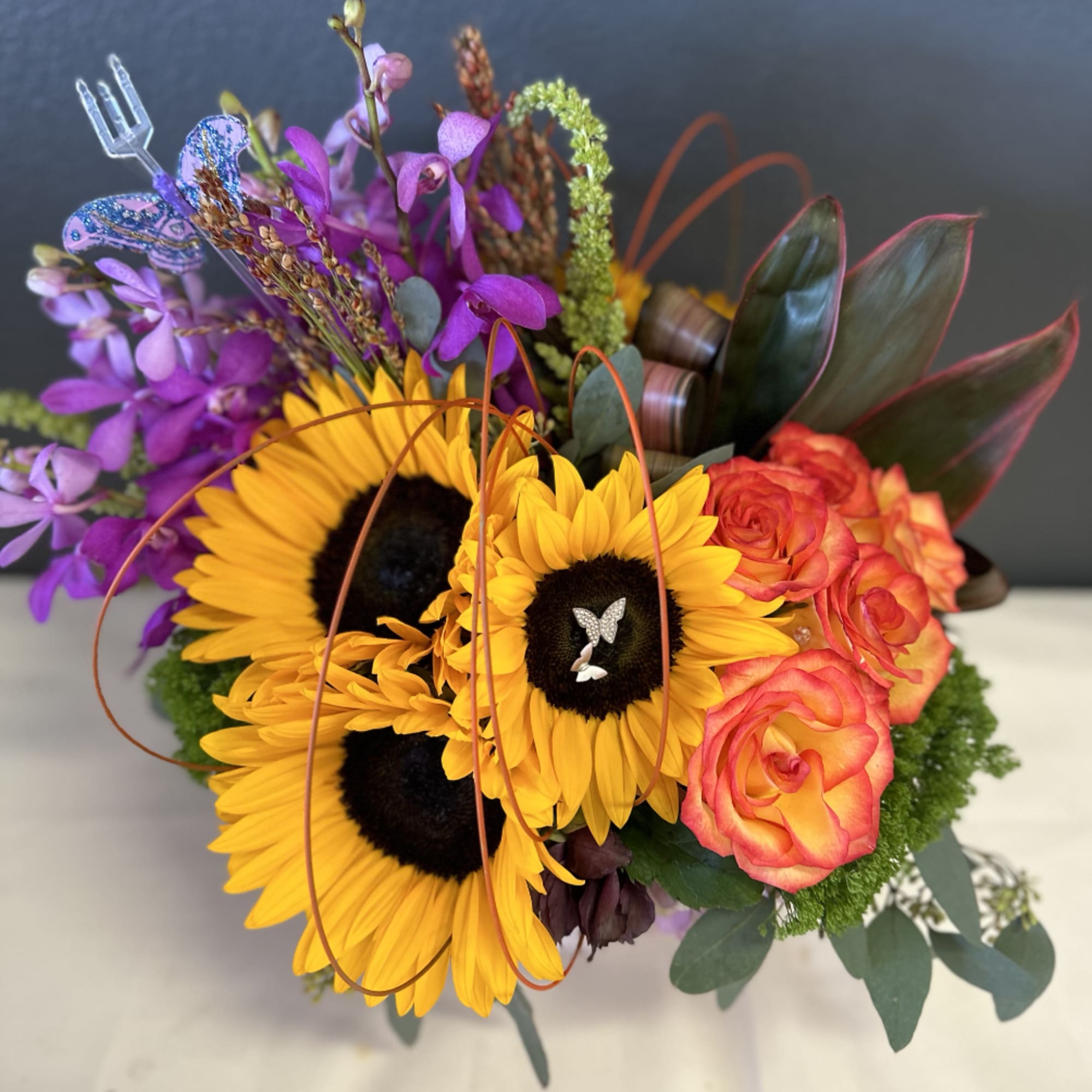 Sunflowers, Orchids, and Roses are uniquely designed in a ceramic vase with