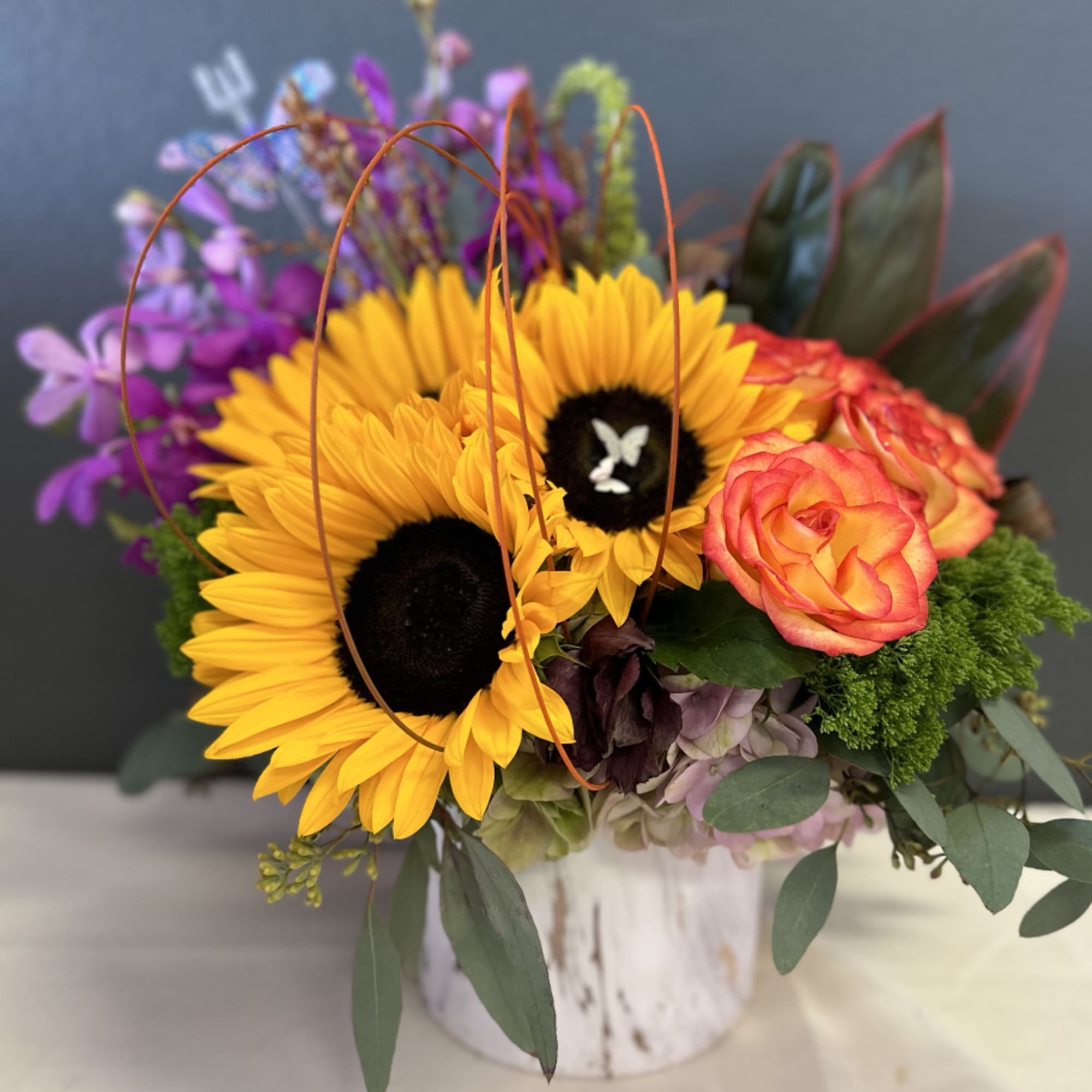 Sunflowers, Orchids, and Roses are uniquely designed in a ceramic vase with