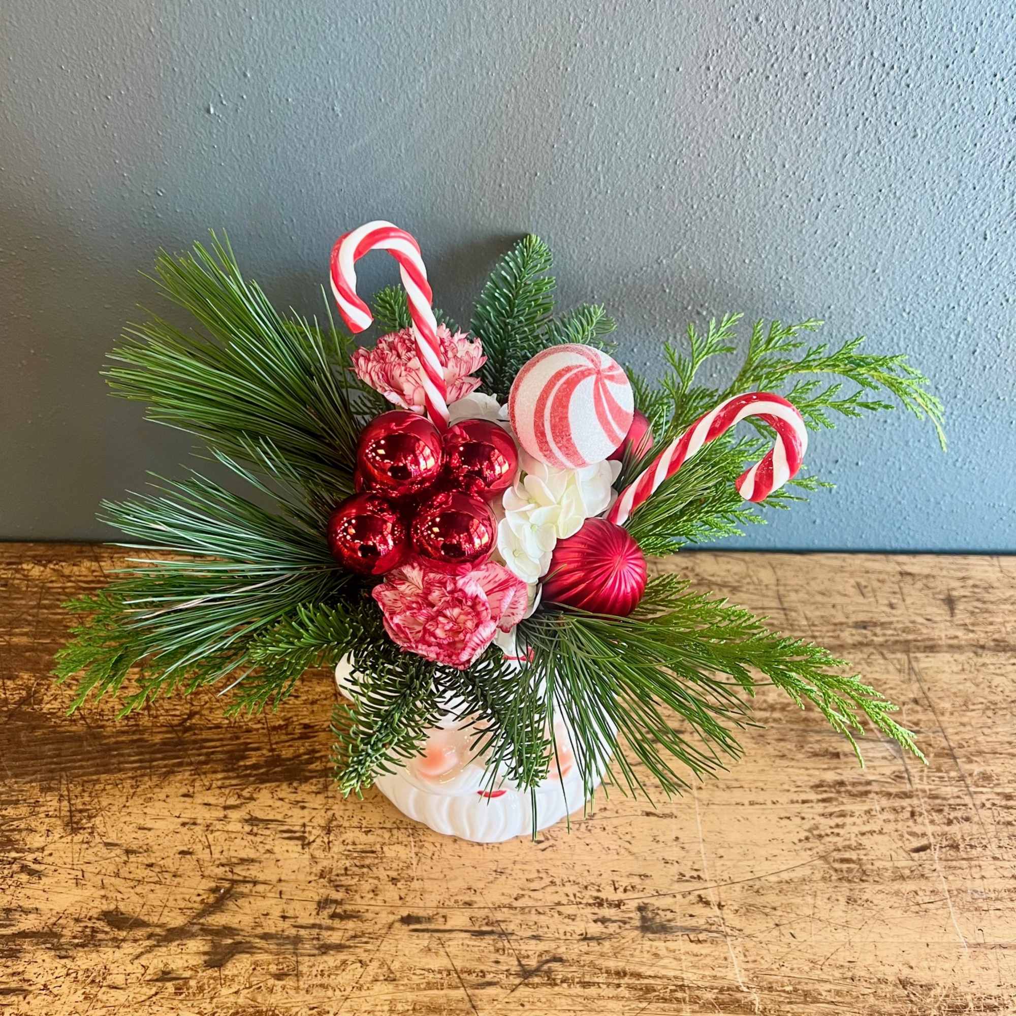A Santa Claus vase overflowing with evergreens, florals, Christmas ornaments with a