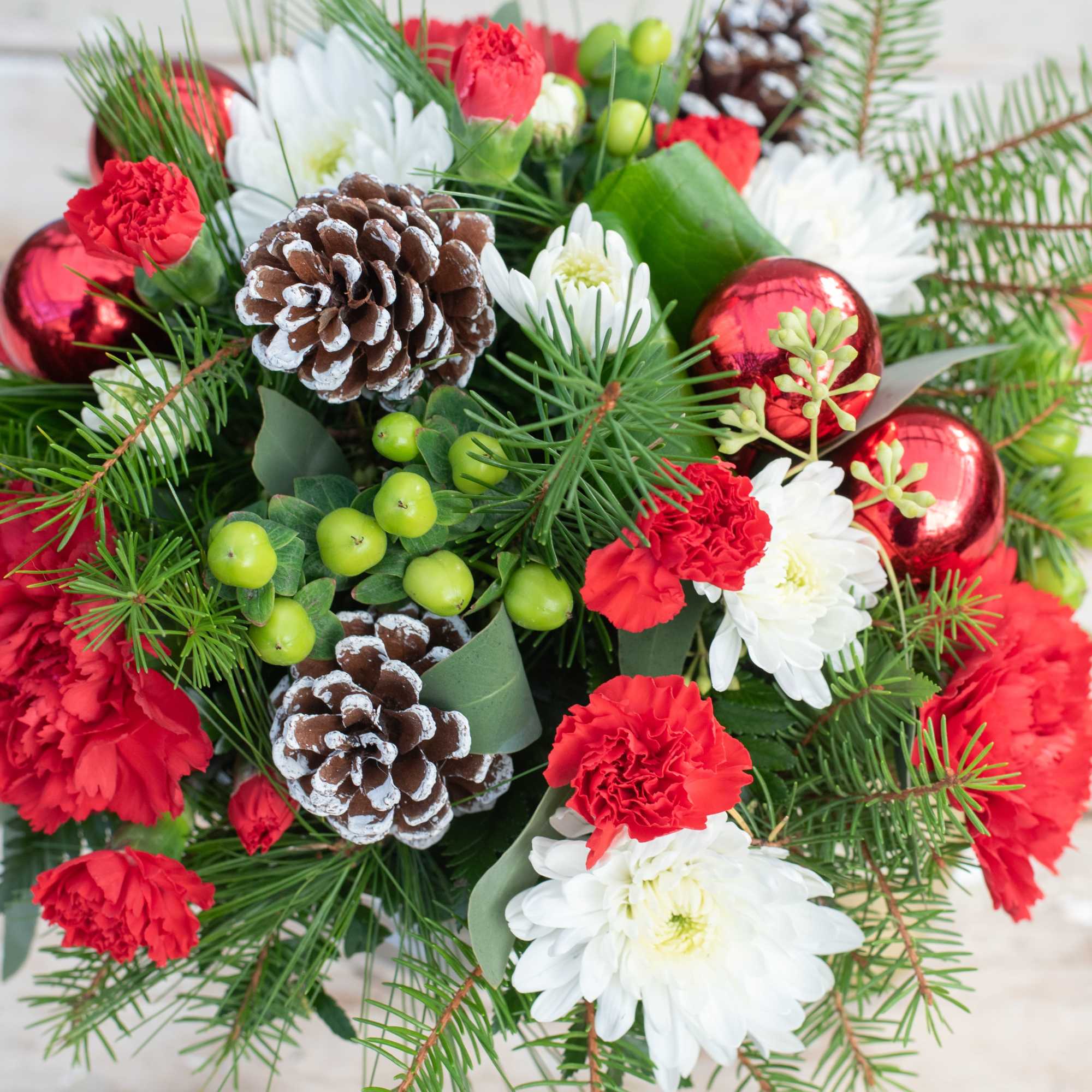 Classic rounded holiday centerpiece filled with  mums, carnatons, pine cones and
