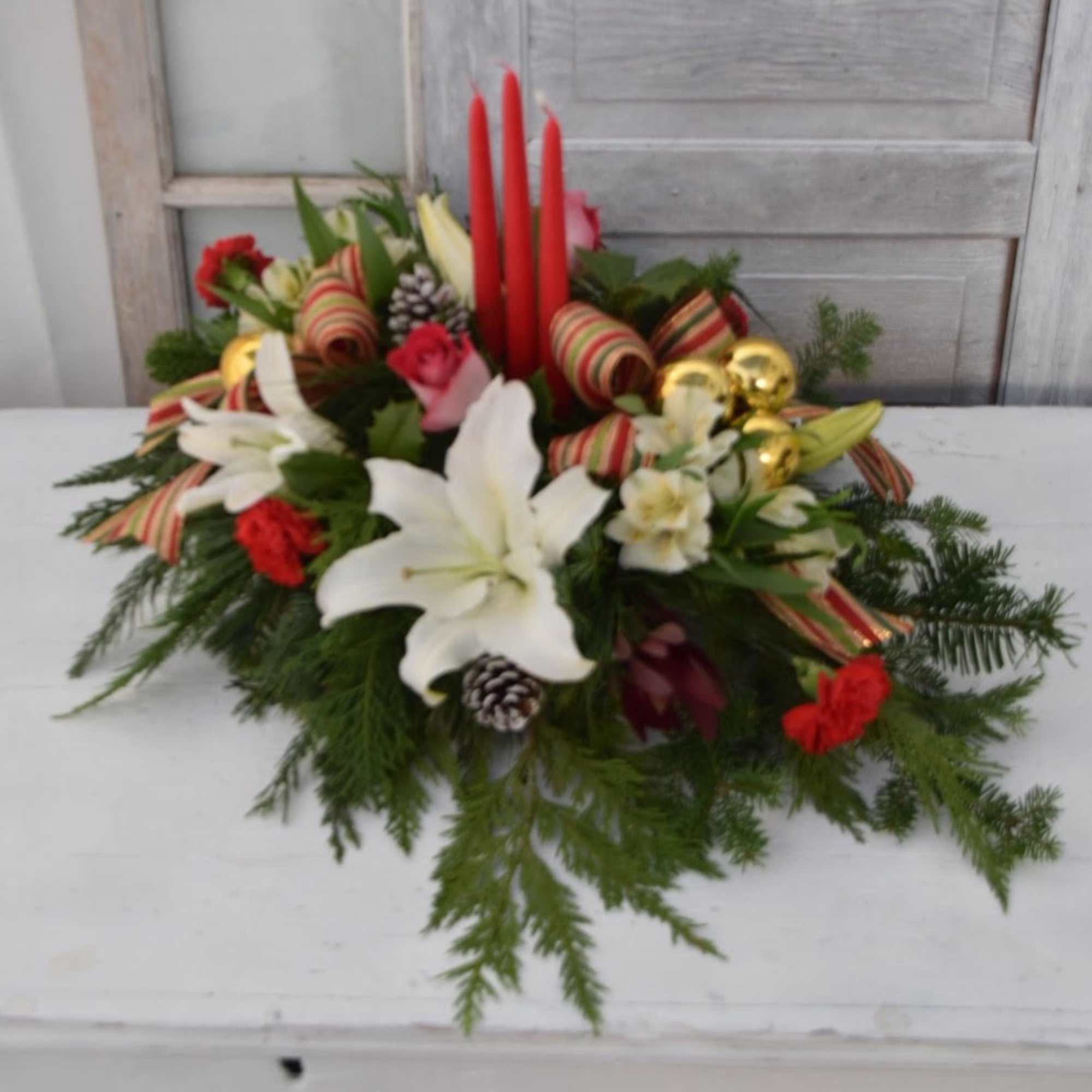 Various priced holiday centerpieces, featuring Christmas greens and holiday hued flowers, in