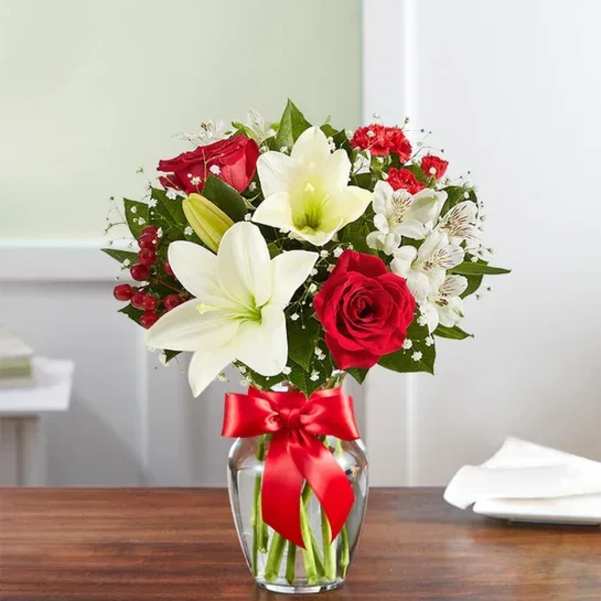 All-around arrangement with red roses and mini carnations; white Asiatic lilies and
