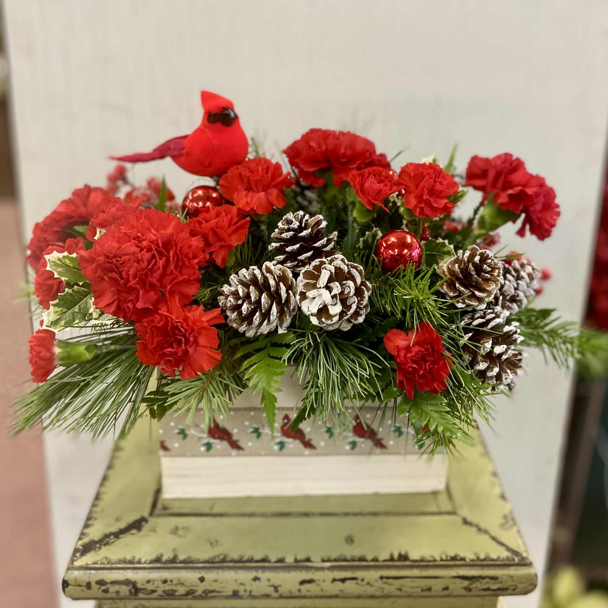 A bright and cheery cardinal sits atop this long lasting floral arrangement