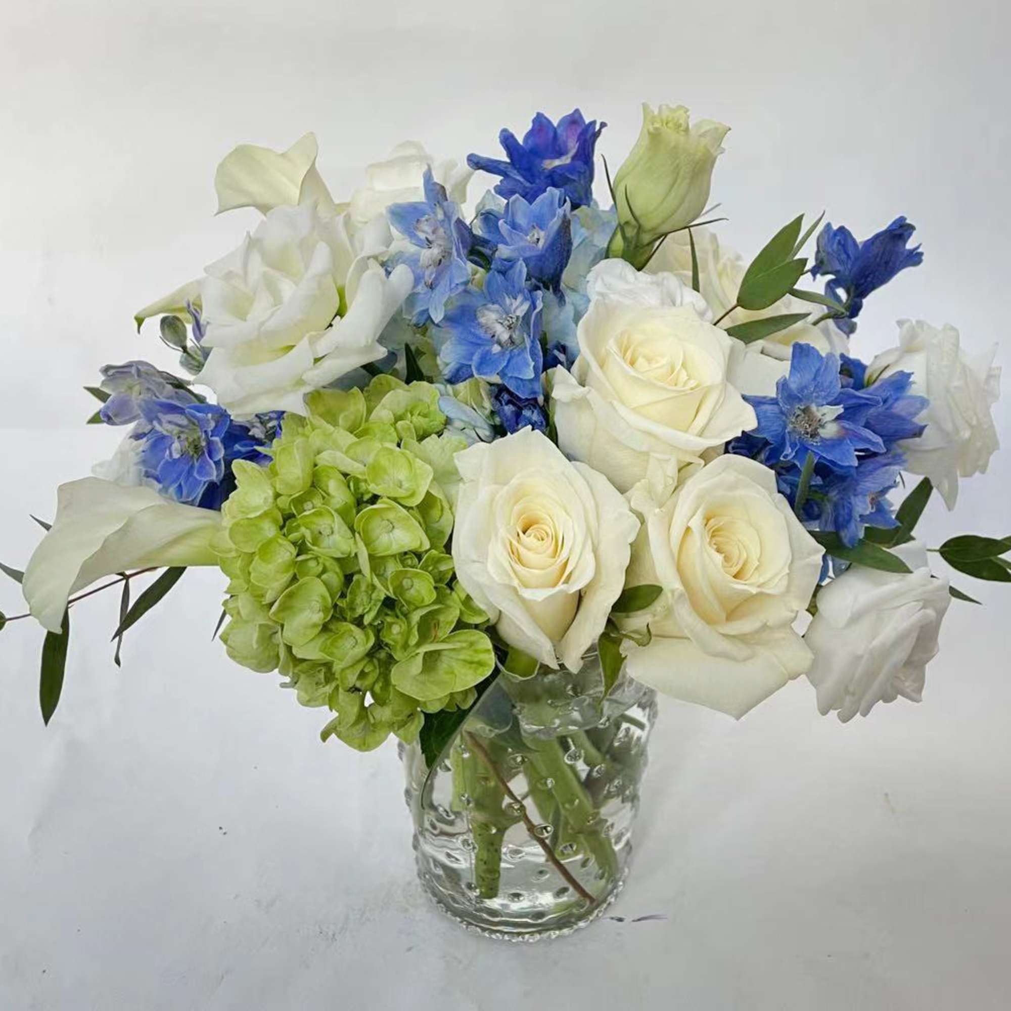 This arrangement stays in white and blue color. It includes white roses