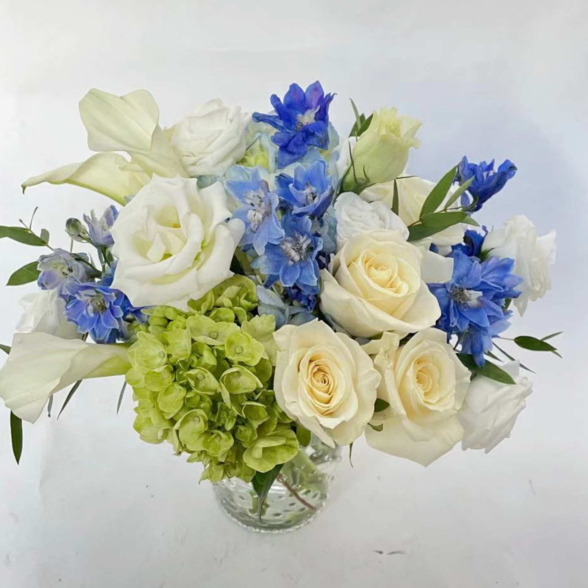 This arrangement stays in white and blue color. It includes white roses