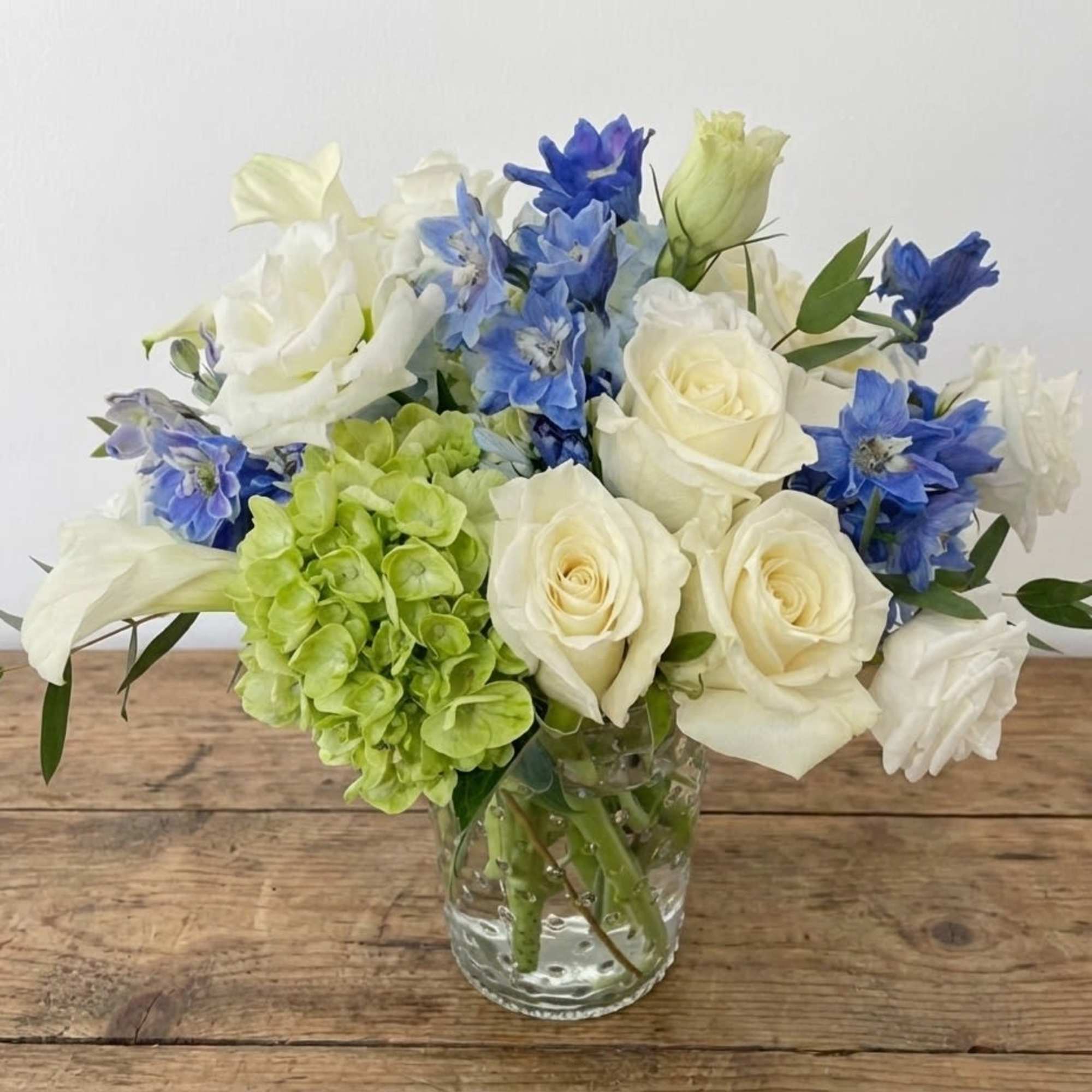 This arrangement stays in white and blue color. It includes white roses
