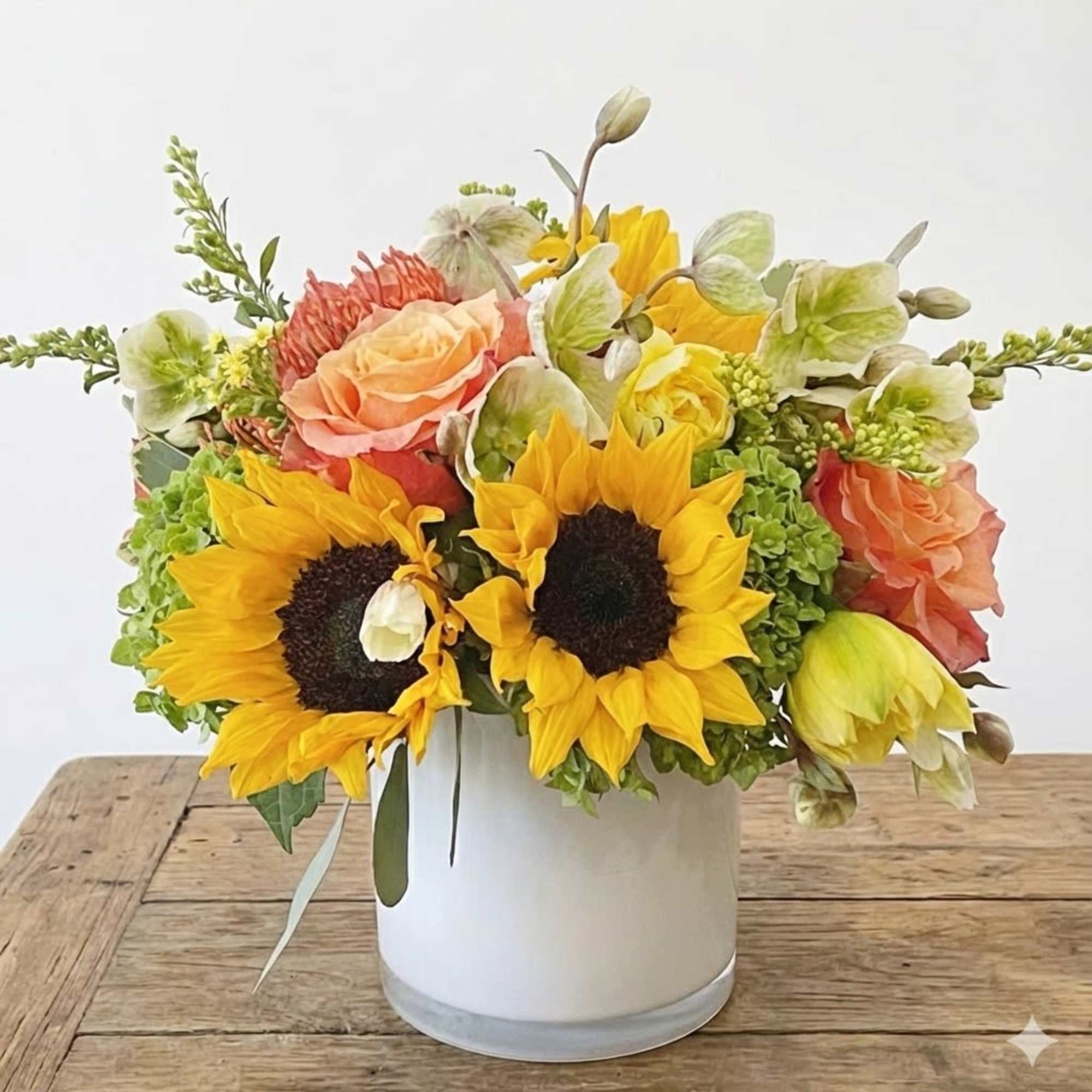 This arrangement include orange free spirit roses, sunflowers, hellebore, hydrangea, daffodils and