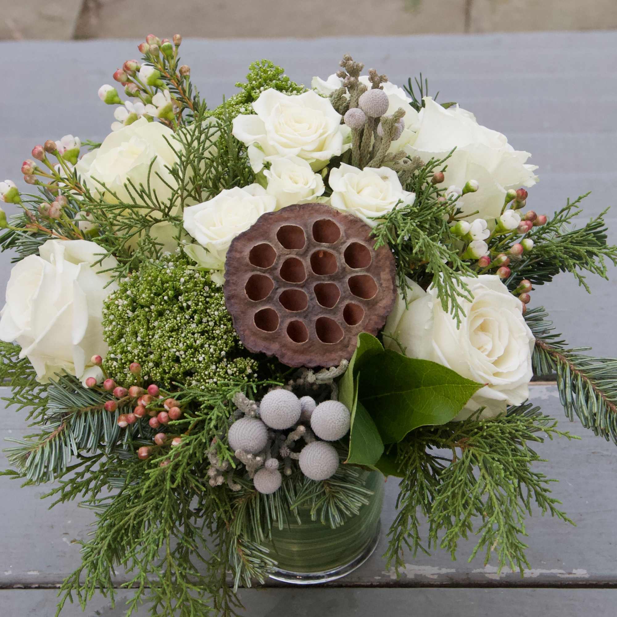 A lovely winter themed arrangement featuring white flowers with evergreens and a