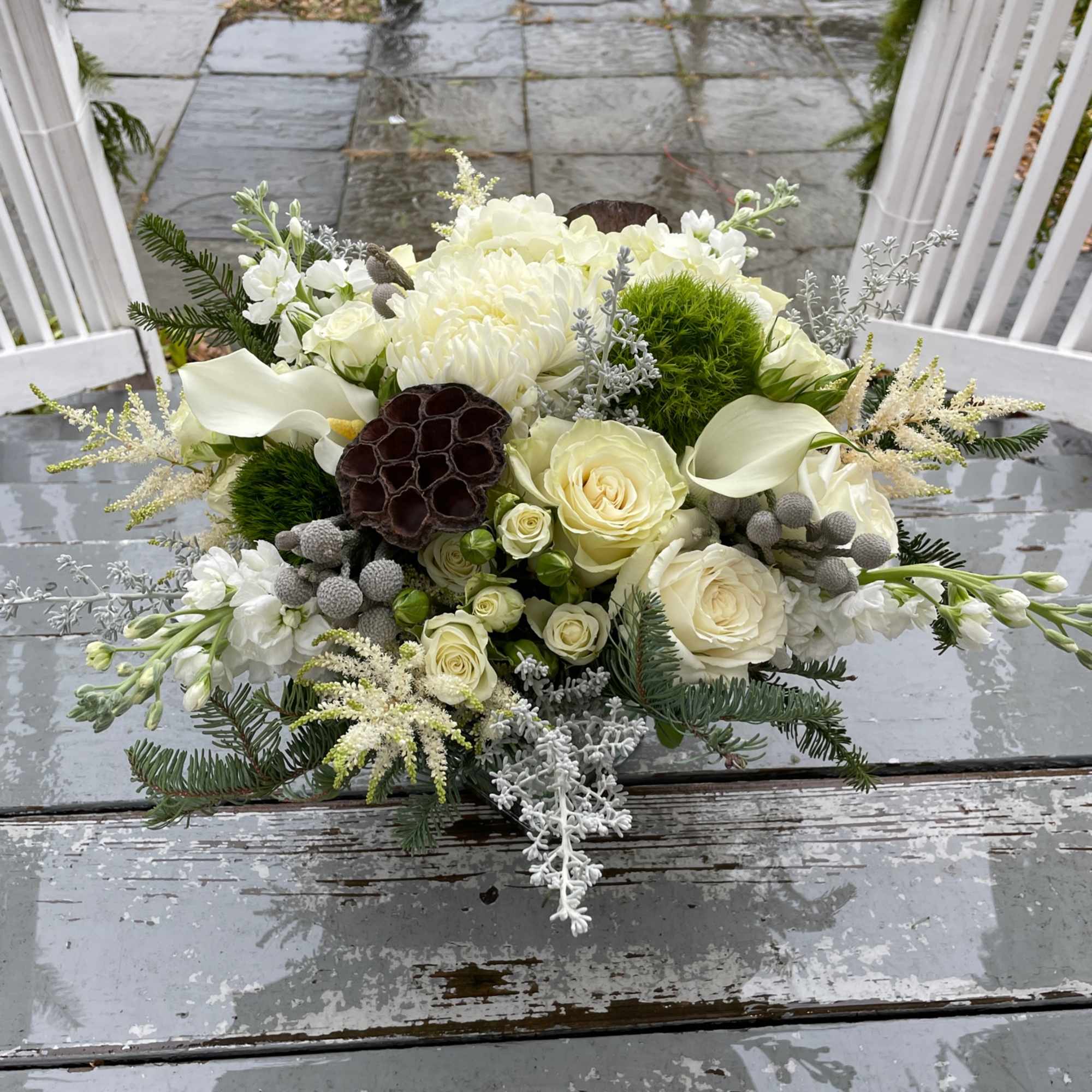 A lovely winter themed arrangement featuring white flowers with evergreens and a