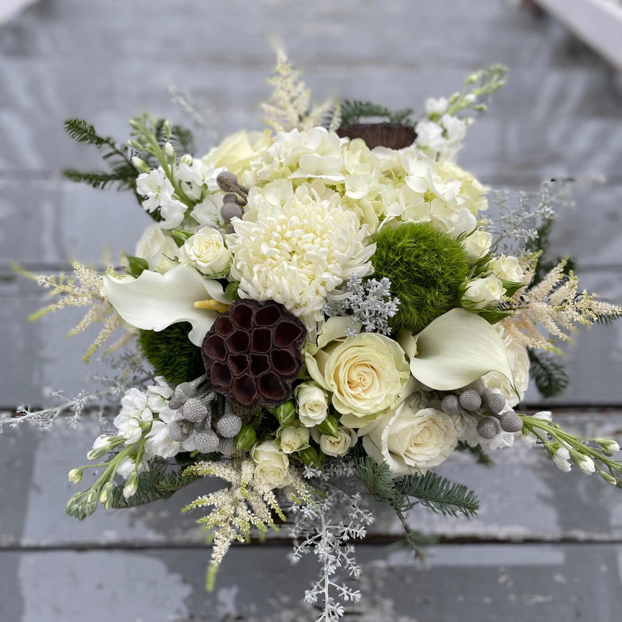A lovely winter themed arrangement featuring white flowers with evergreens and a
