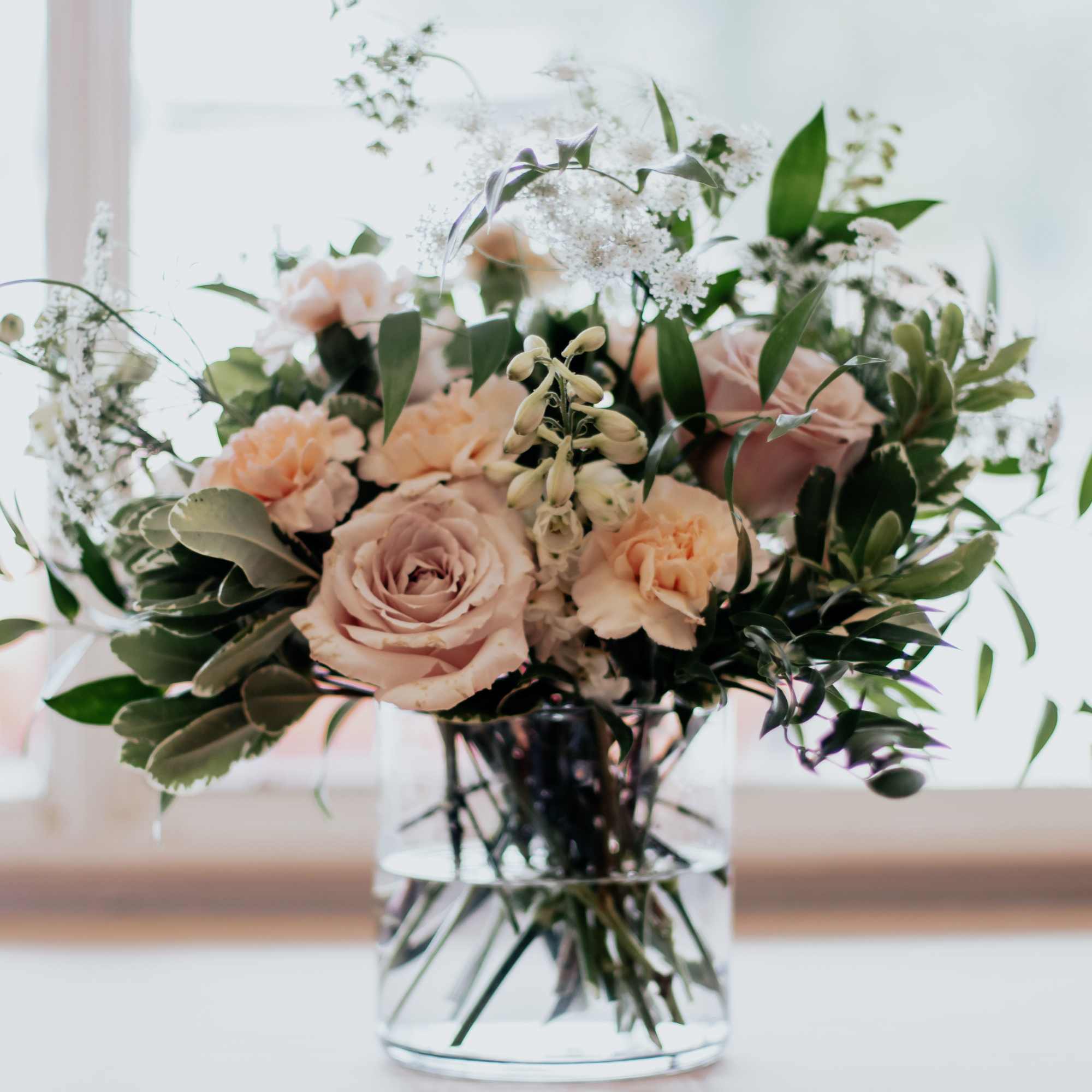 Blushing, whimsical arrangement with greenery. Containing roses, carnations, delphiniums &amp; 
