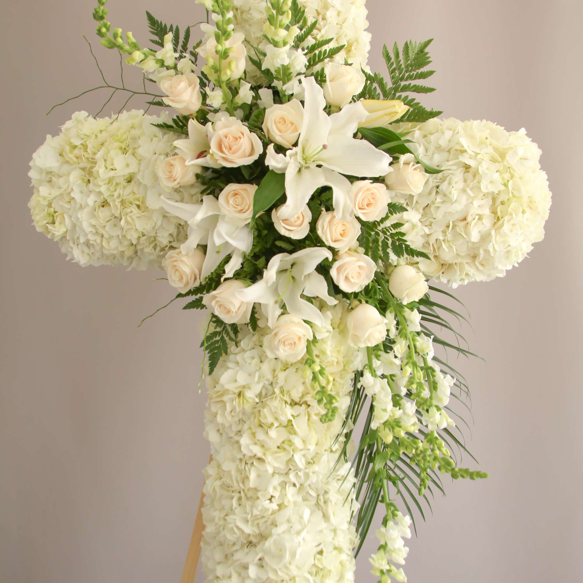 A white cross with Hydrangeas, roses, and greens. 