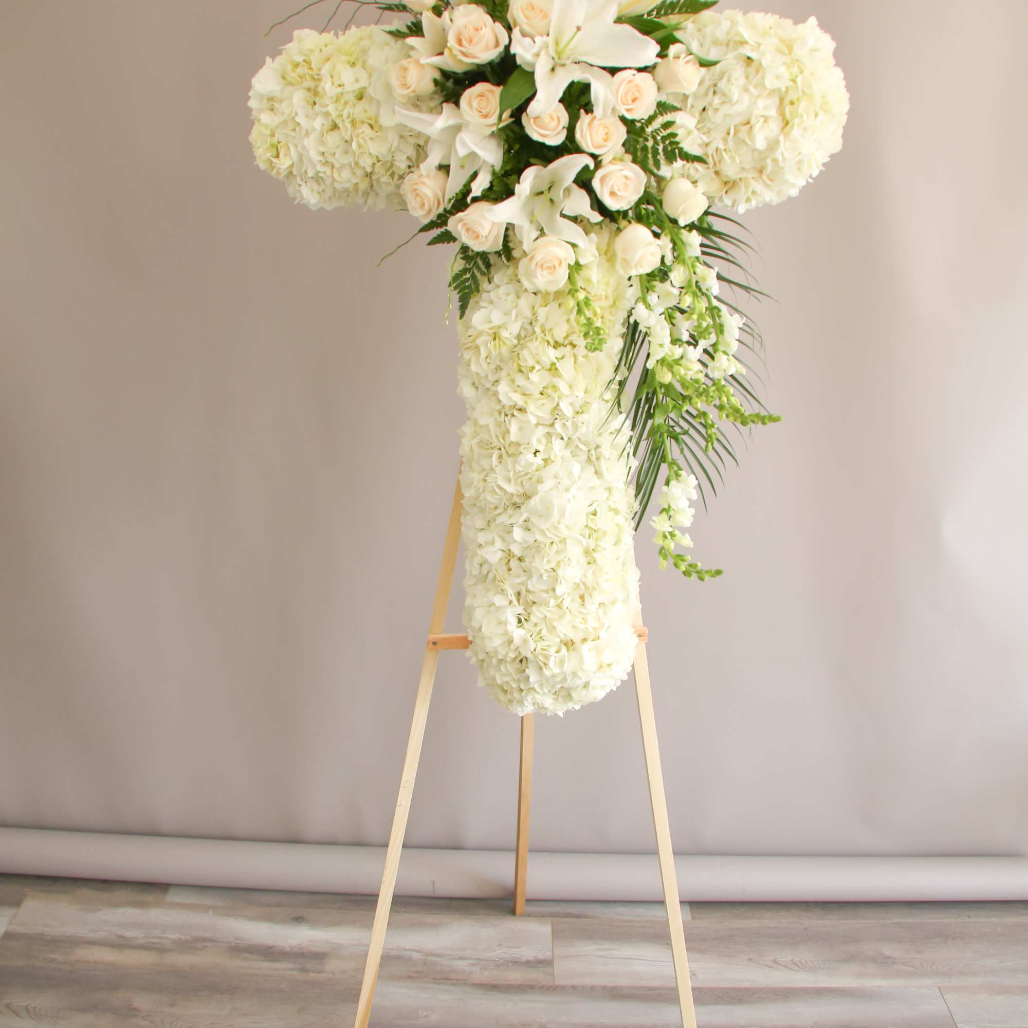 A white cross with Hydrangeas, roses, and greens. 