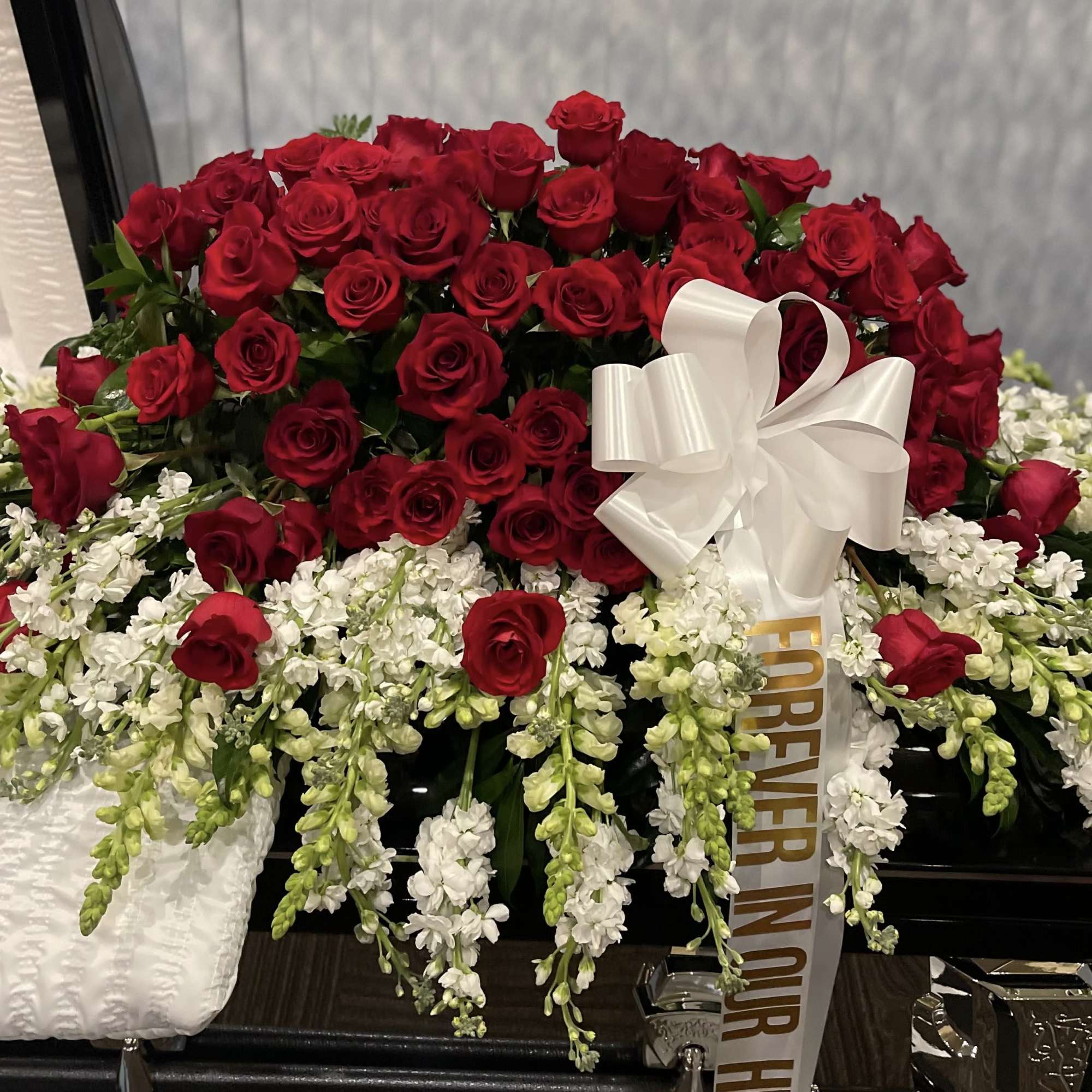 Red roses and white flowers in this full casket symbolize love and