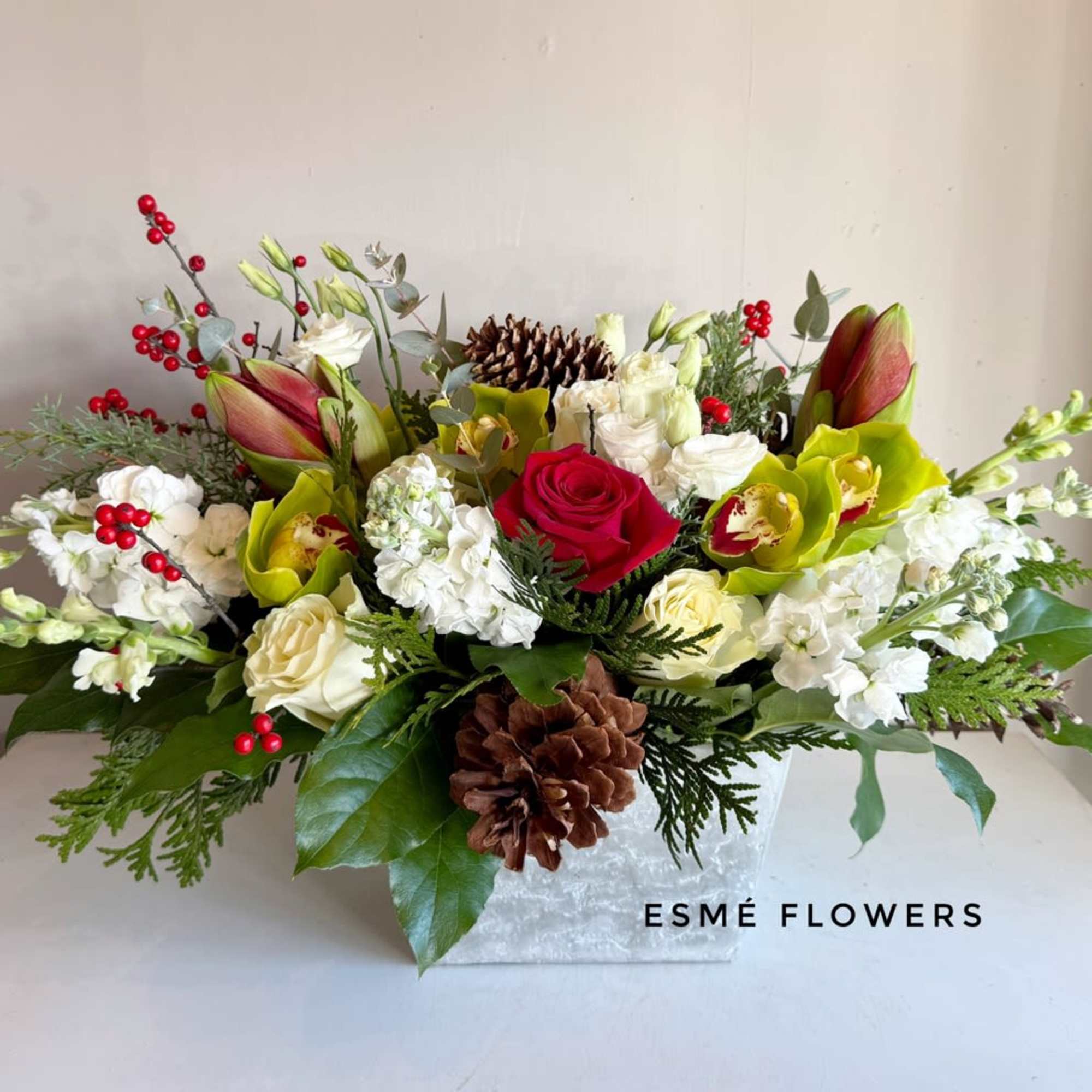 A low and long, premium centerpiece featuring Amaryllis, Cymbidium orchids, roses, lisianthus