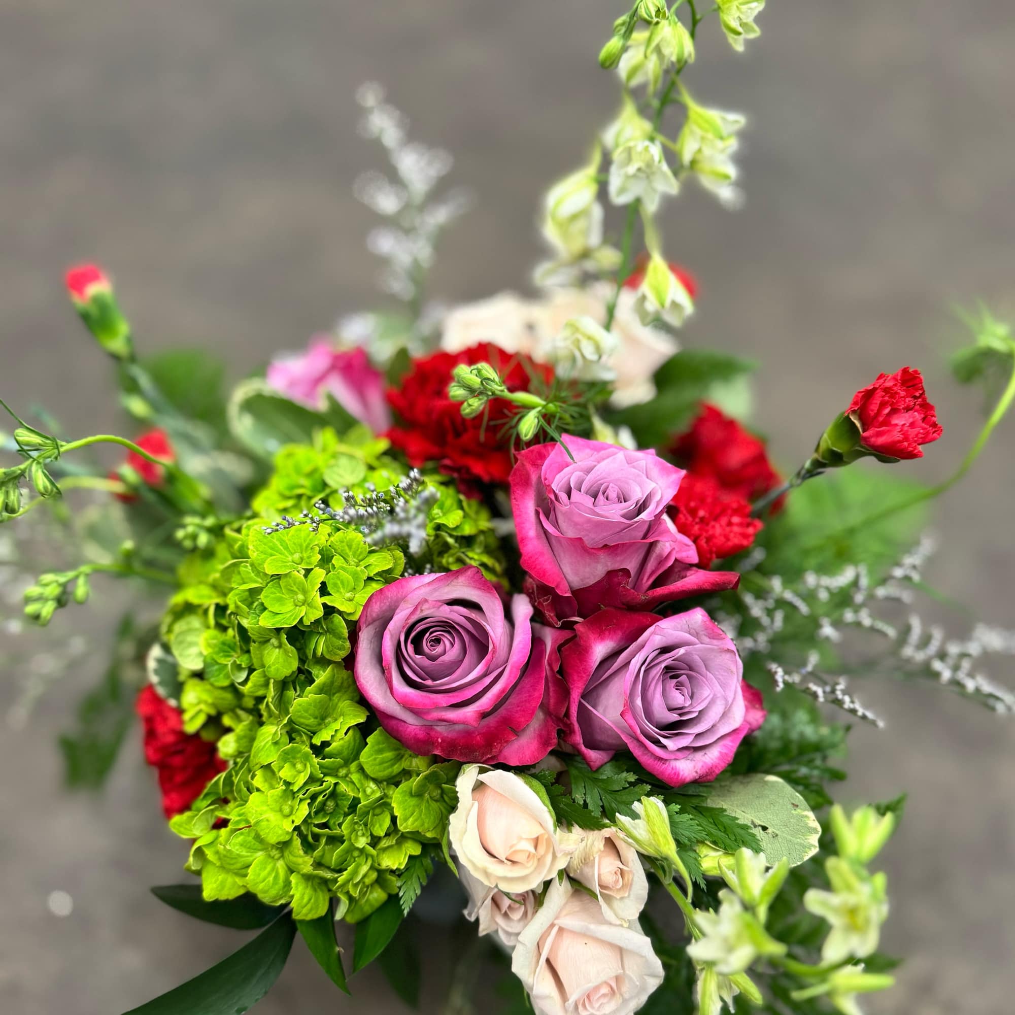 A lush blend of lavender roses, rich red carnations, green hydrangea, blush