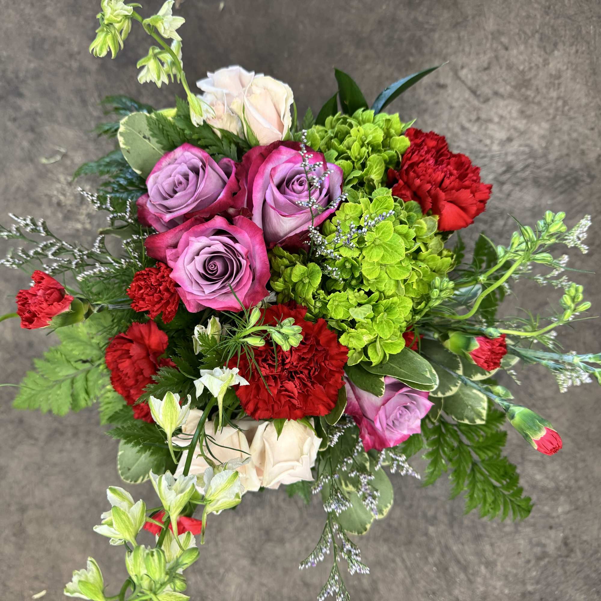 A lush blend of lavender roses, rich red carnations, green hydrangea, blush