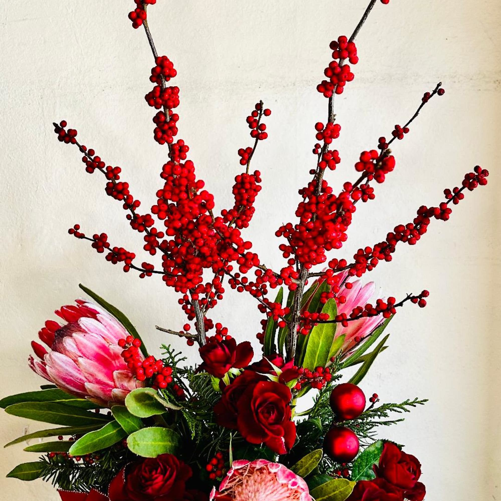 Towering Ilex berries, textured protea, red roses, lush greenery decorated for Christmas