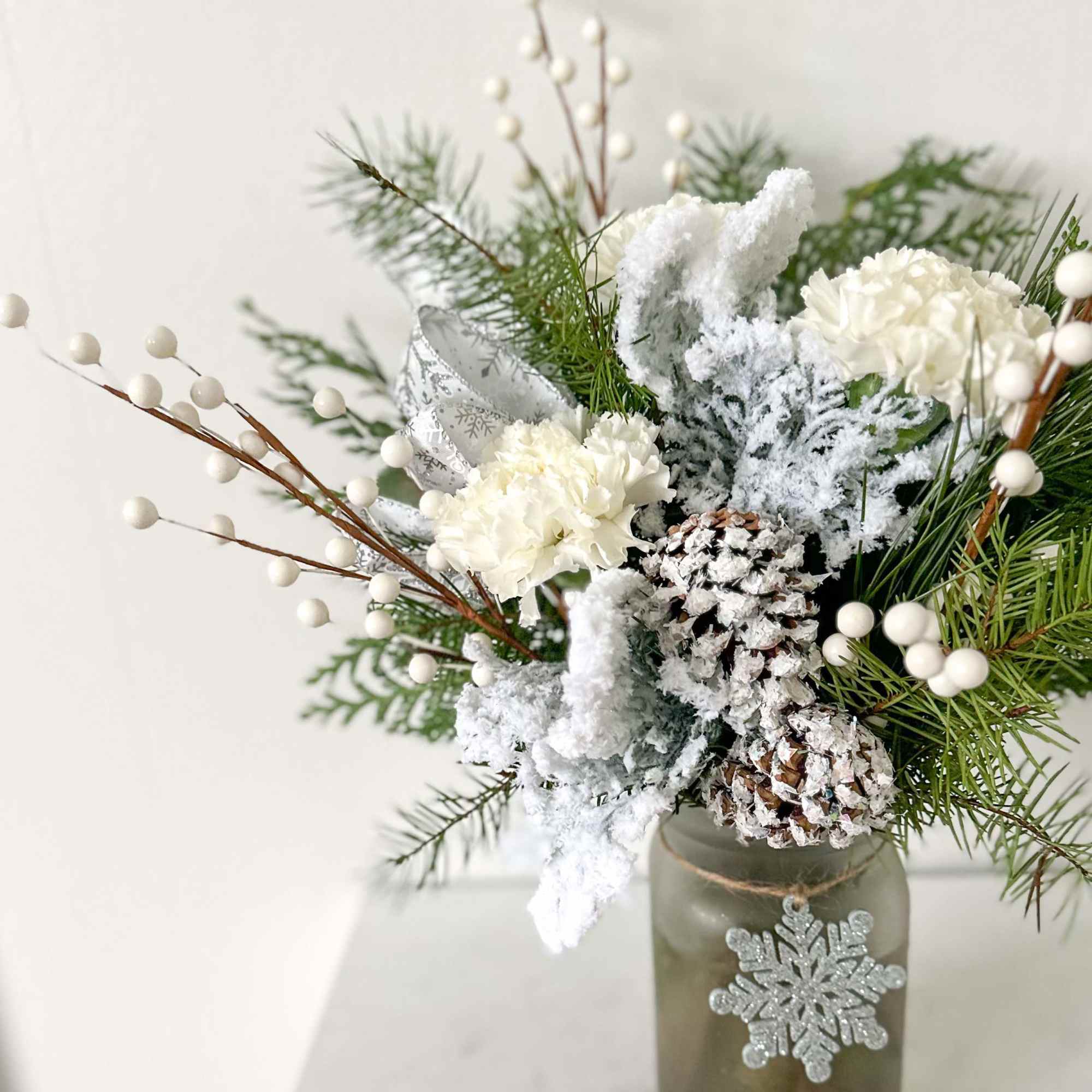 A snowy arrangement full of winter greens with a snowflake ornament. 