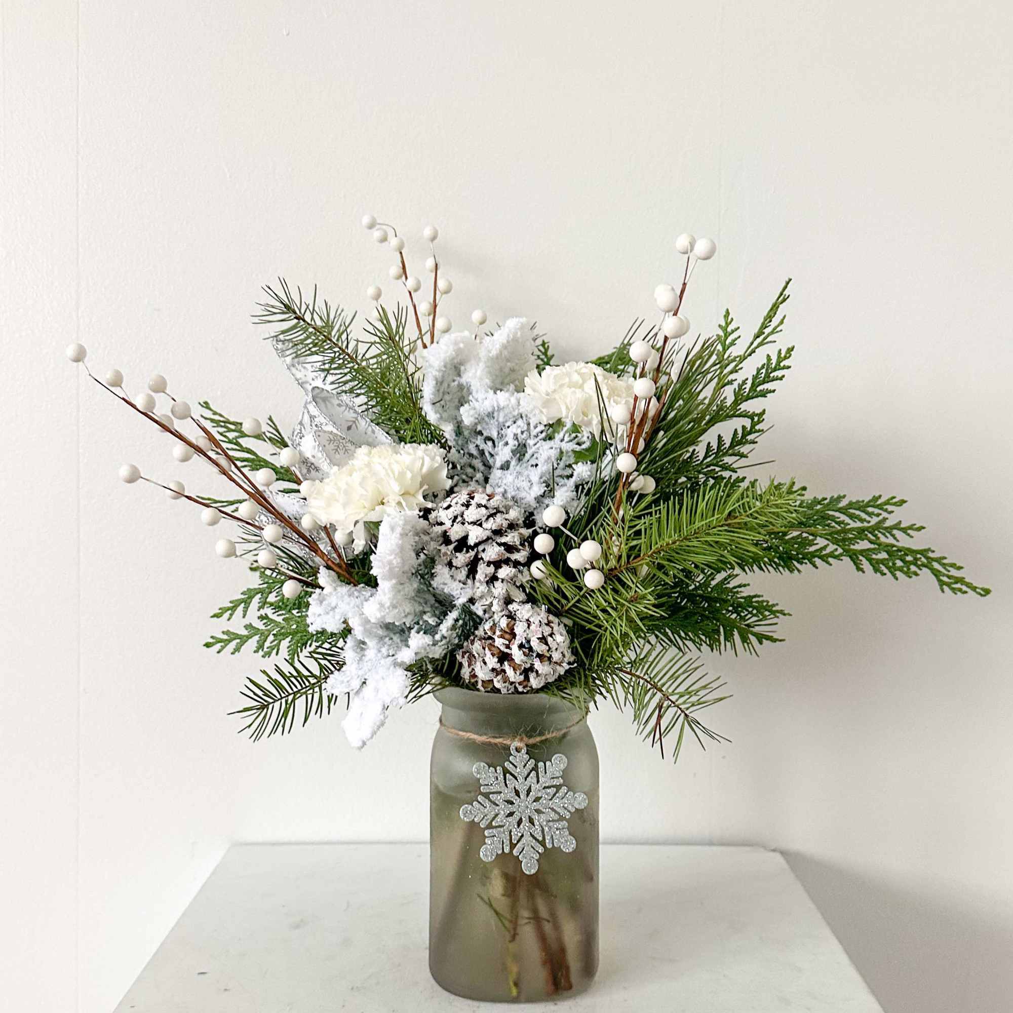 A snowy arrangement full of winter greens with a snowflake ornament. 