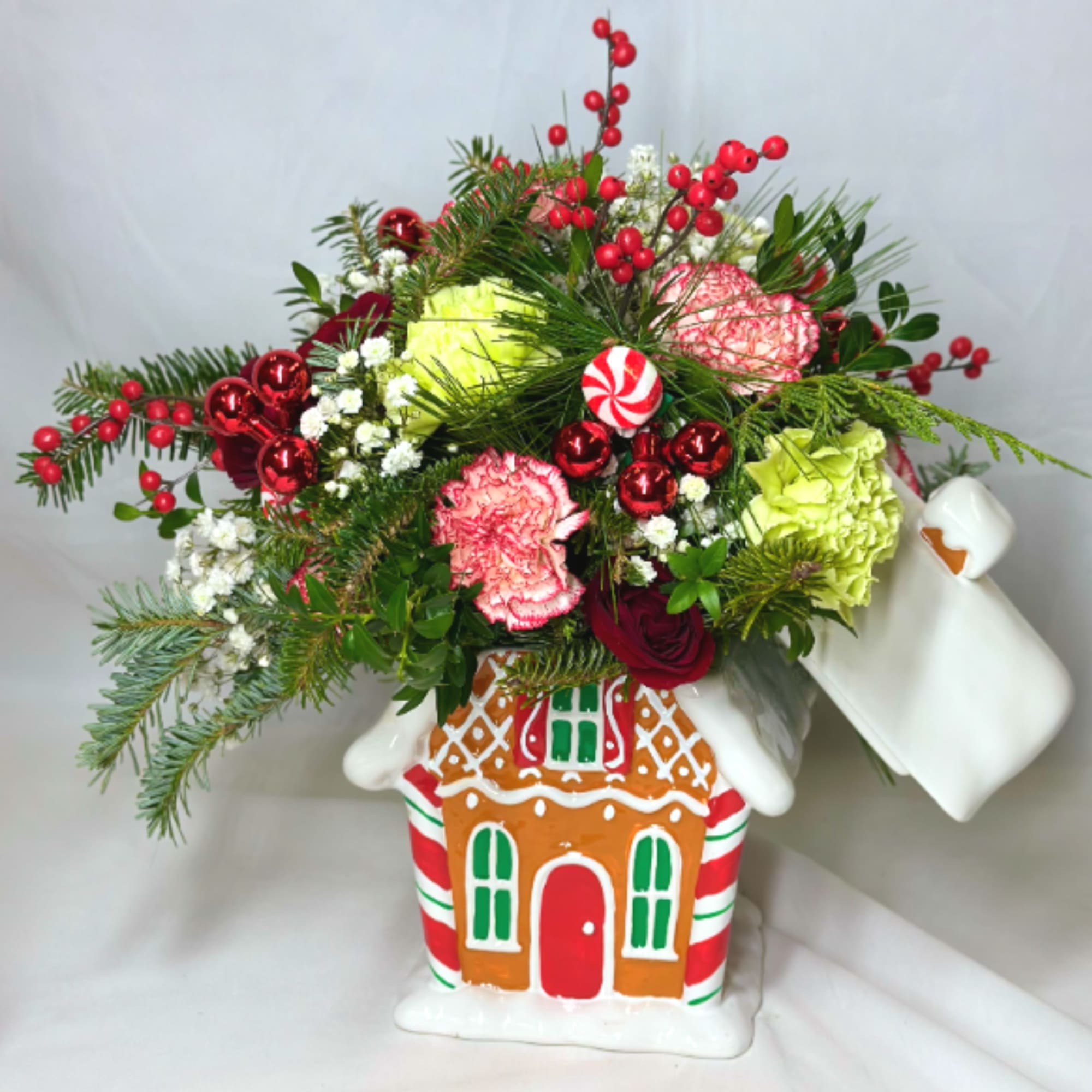 This delightful Christmas arrangement features a reusable Gingerbread house container vase, adorned