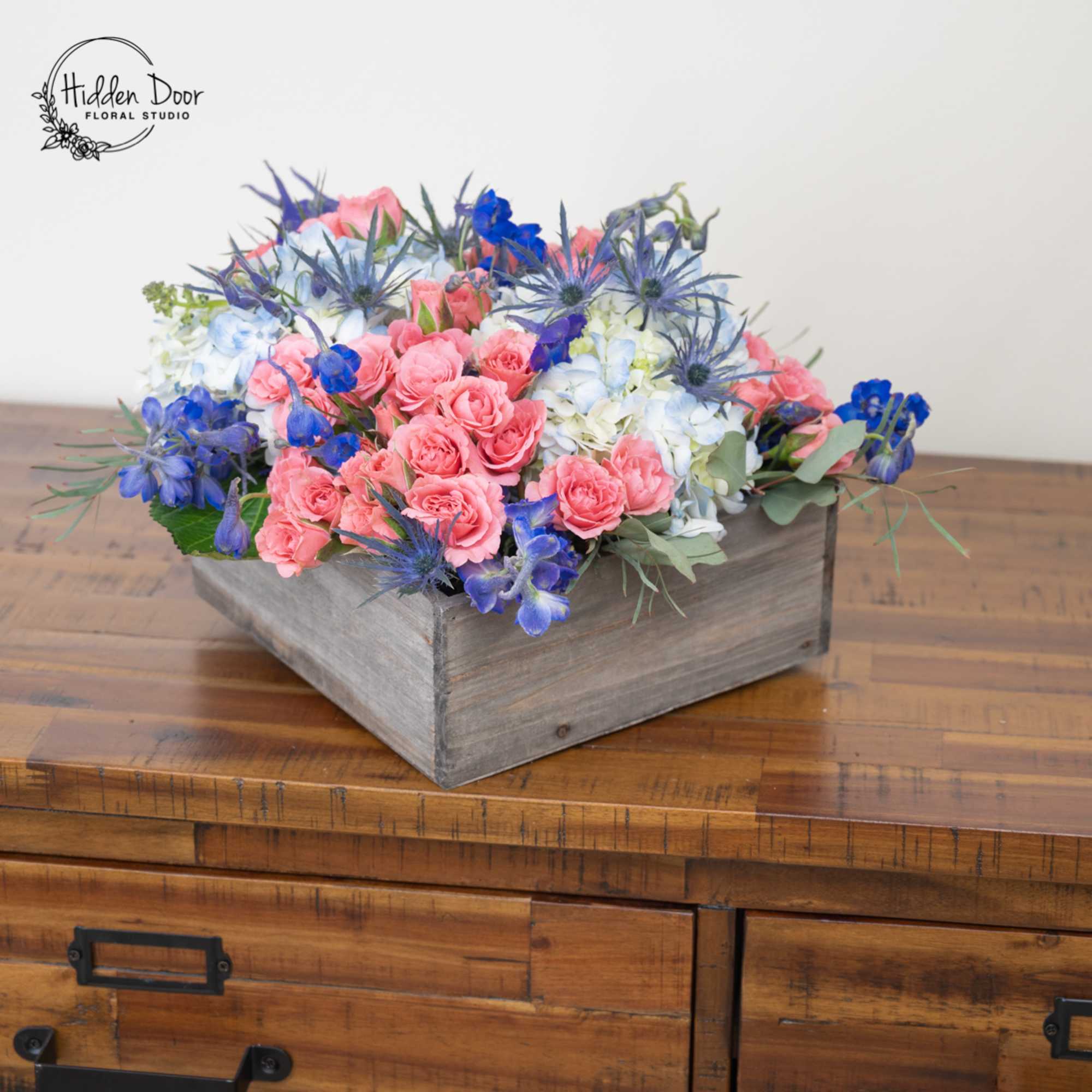 Coral is a fresh, vibrant arrangement blending soft peach roses, blue accents