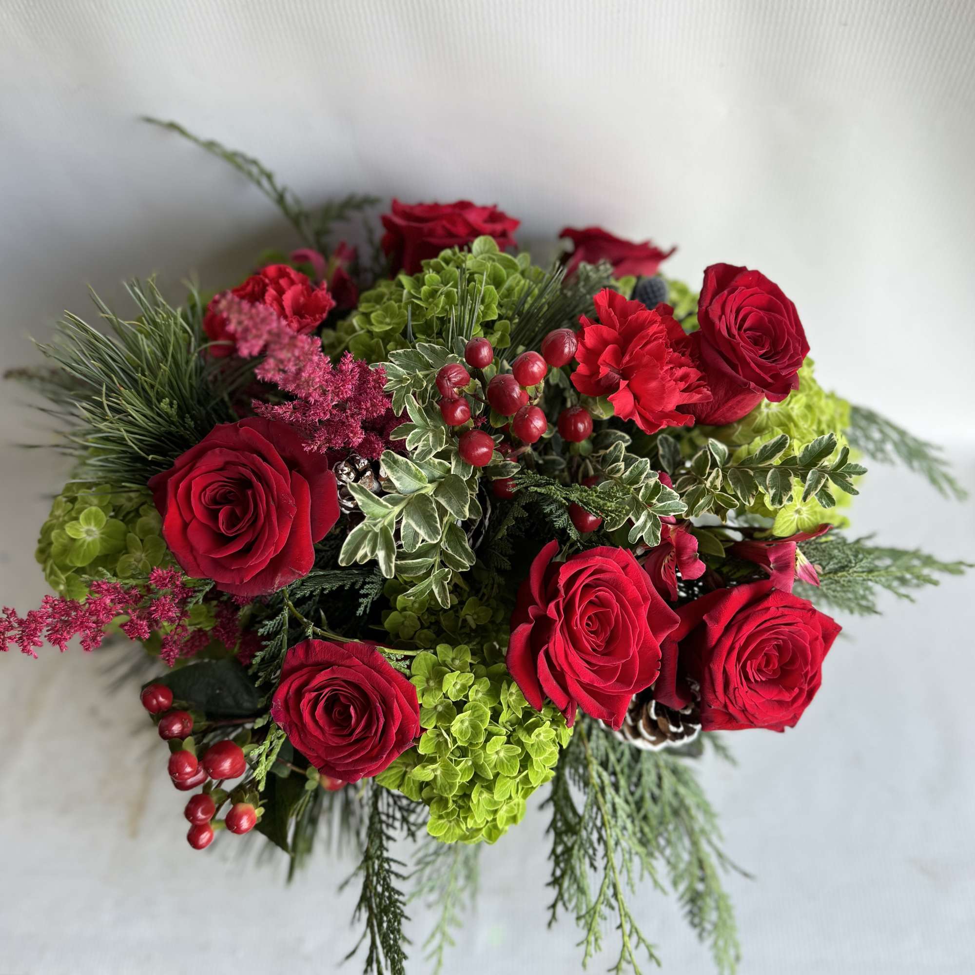 Red roses, green hydrangeas, blue thistle, seeded eucalyptus and hanging amaranths fill