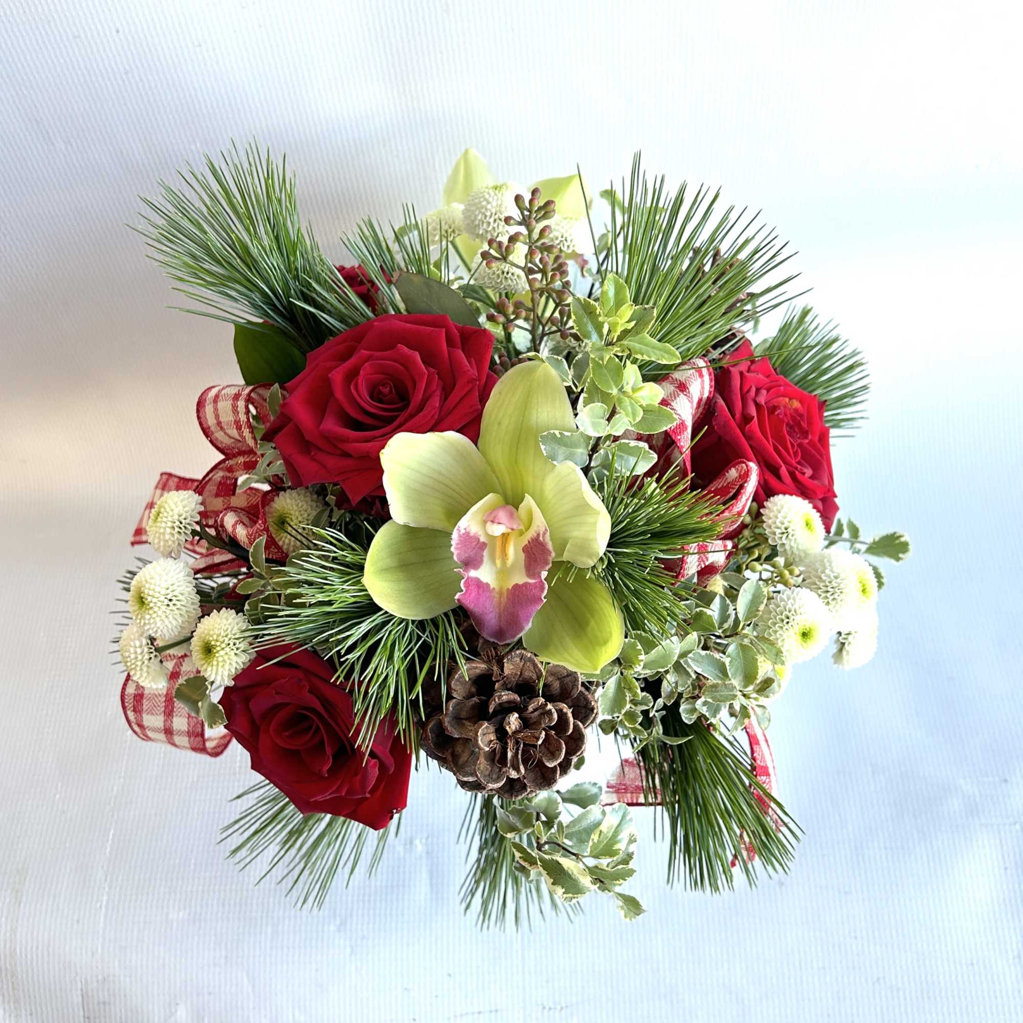 A statement piece with holiday greenery, red roses and orchids including a