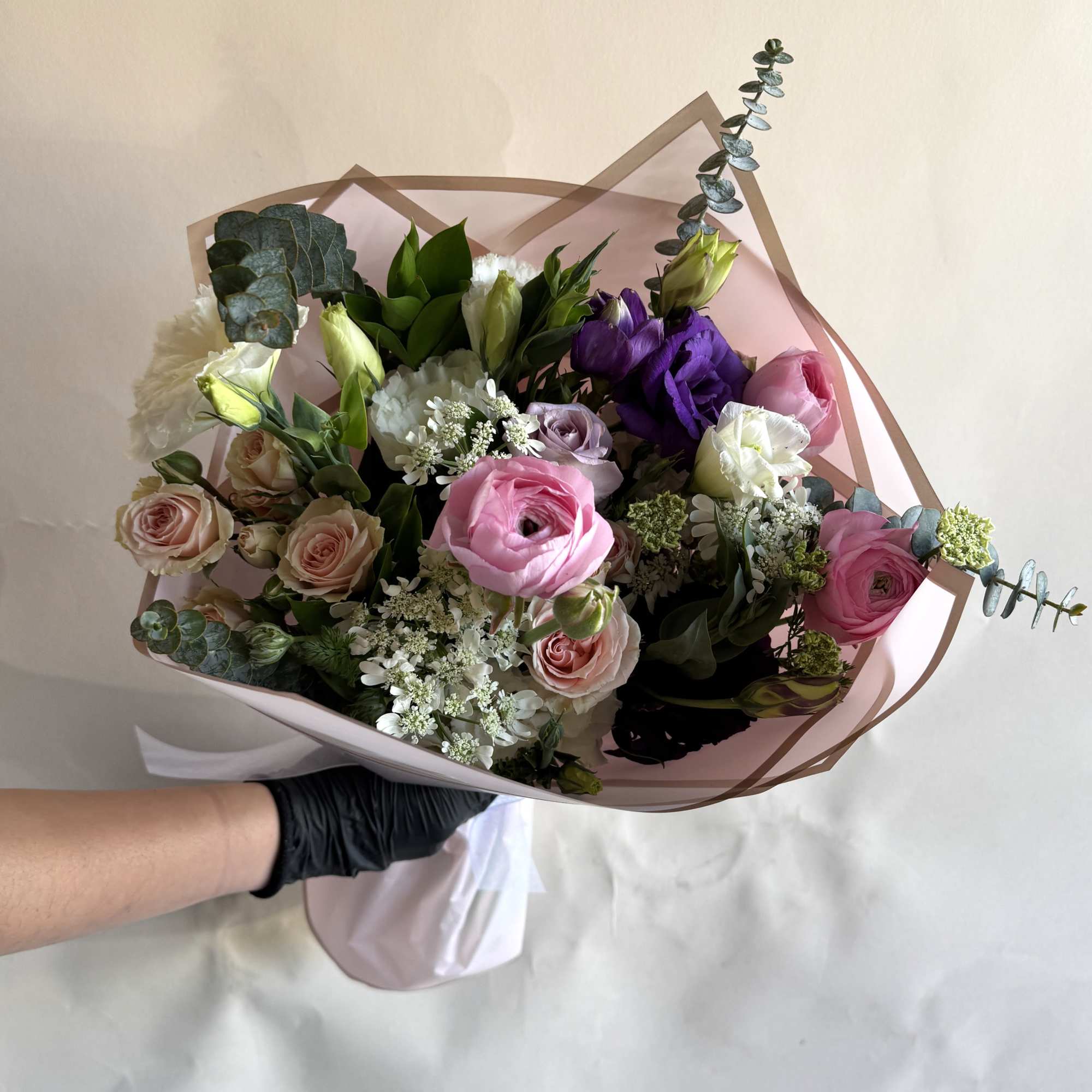 Mix of roses, ranunculus, and lisianthus wrapped in paper with a beautiful