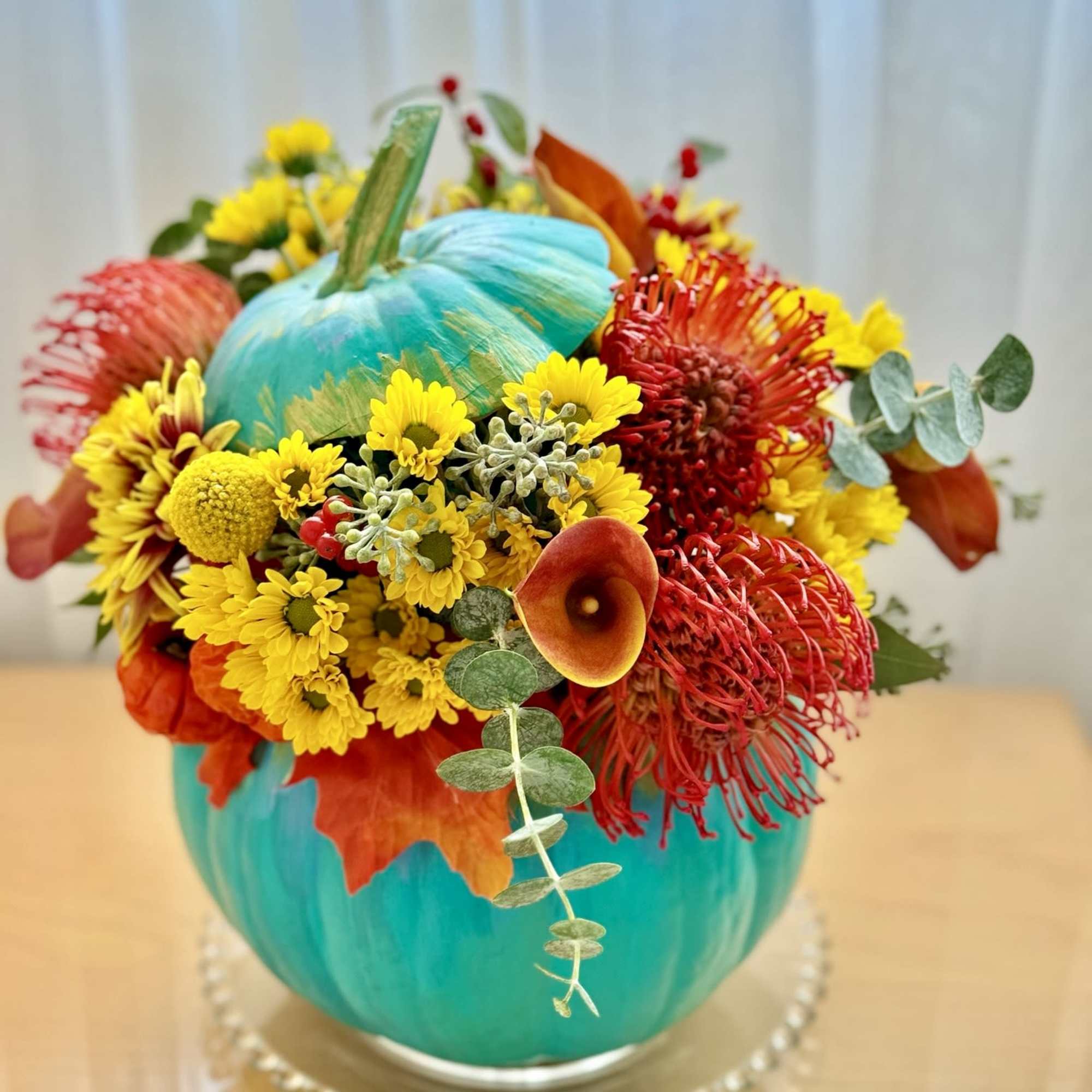 This vibrant and playful fall arrangement is designed in a stunning turquoise