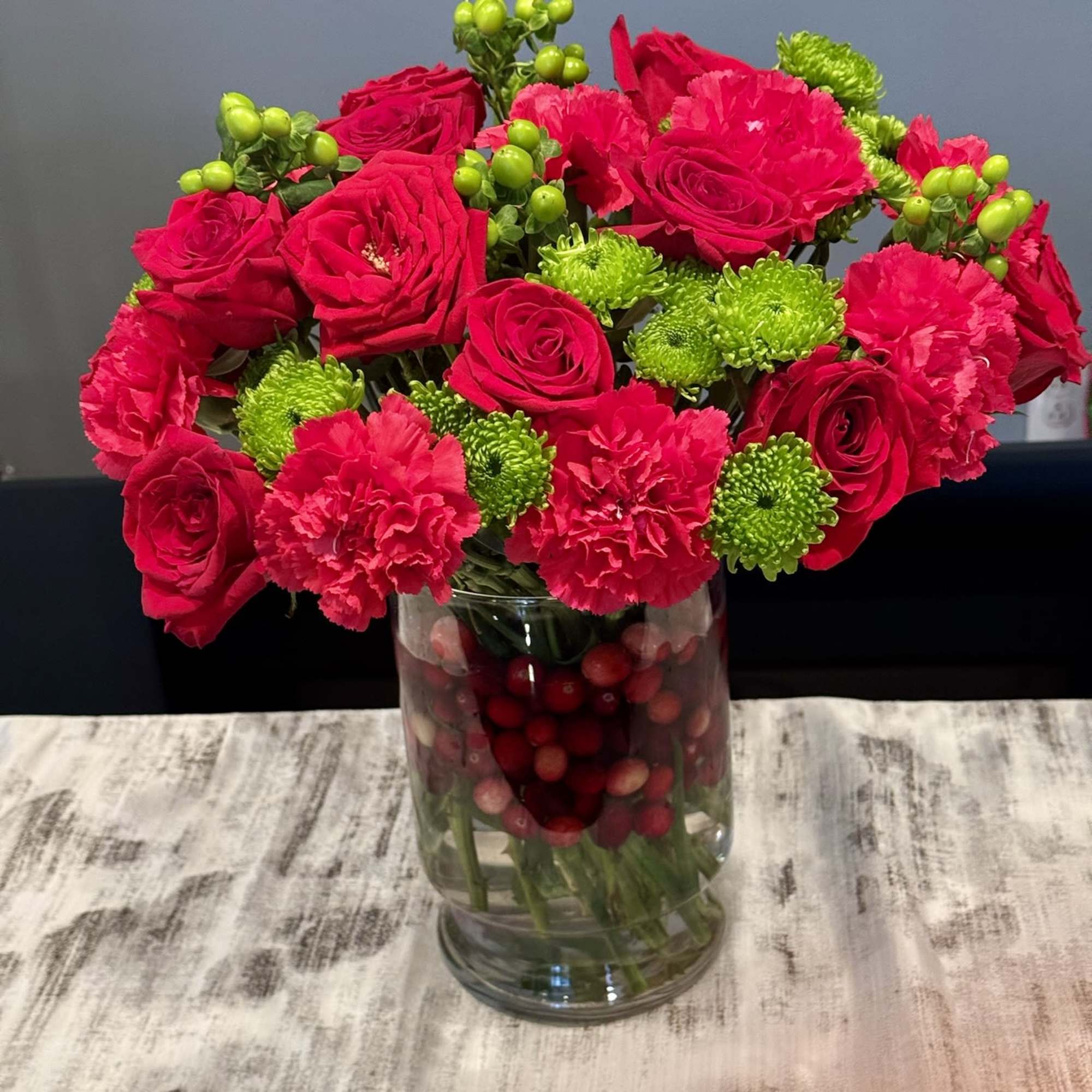 This vibrant arrangement combines rich red roses, crimson carnations, and pops of