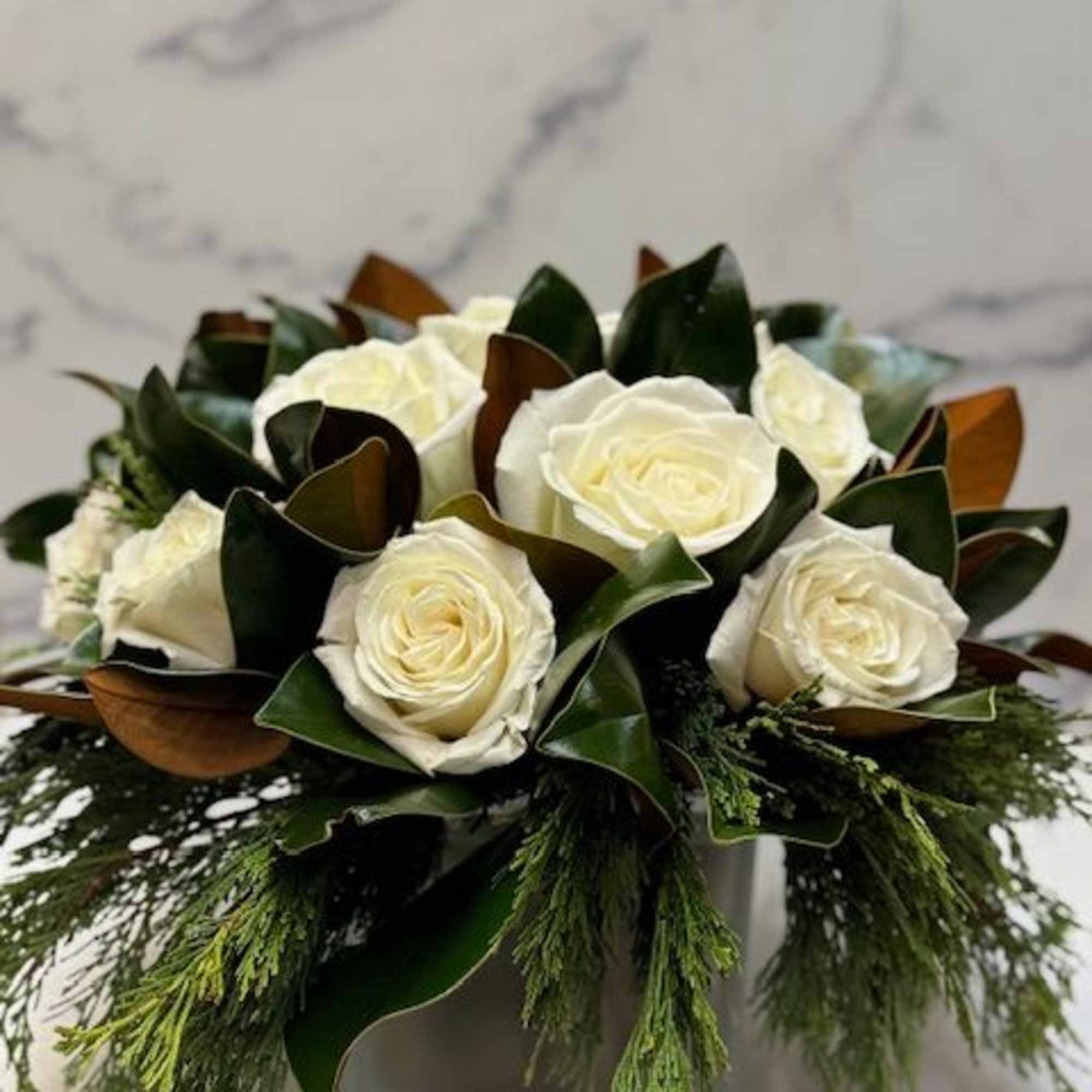 Arrangement filled with winter greens, magnolia, and white roses
