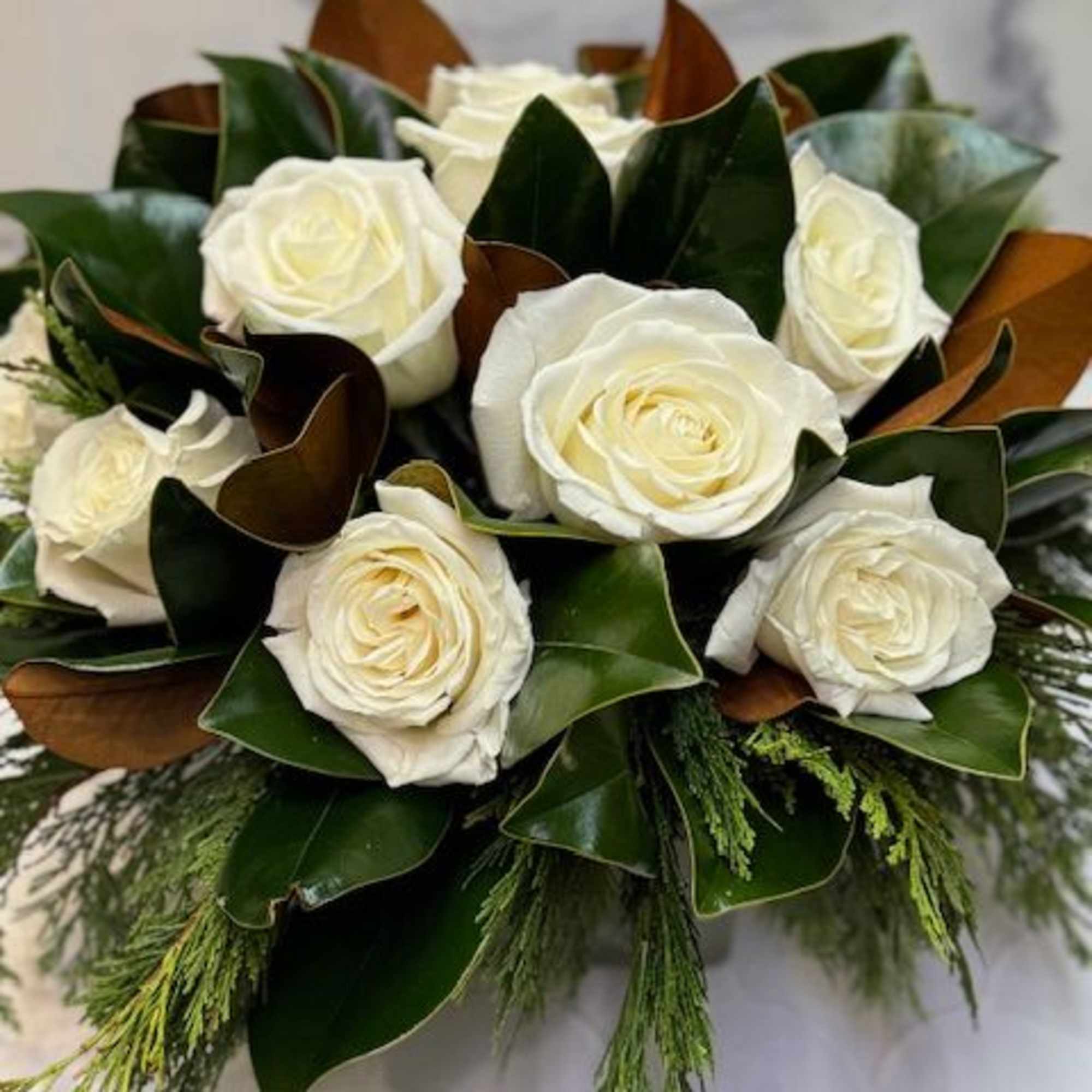 Arrangement filled with winter greens, magnolia, and white roses