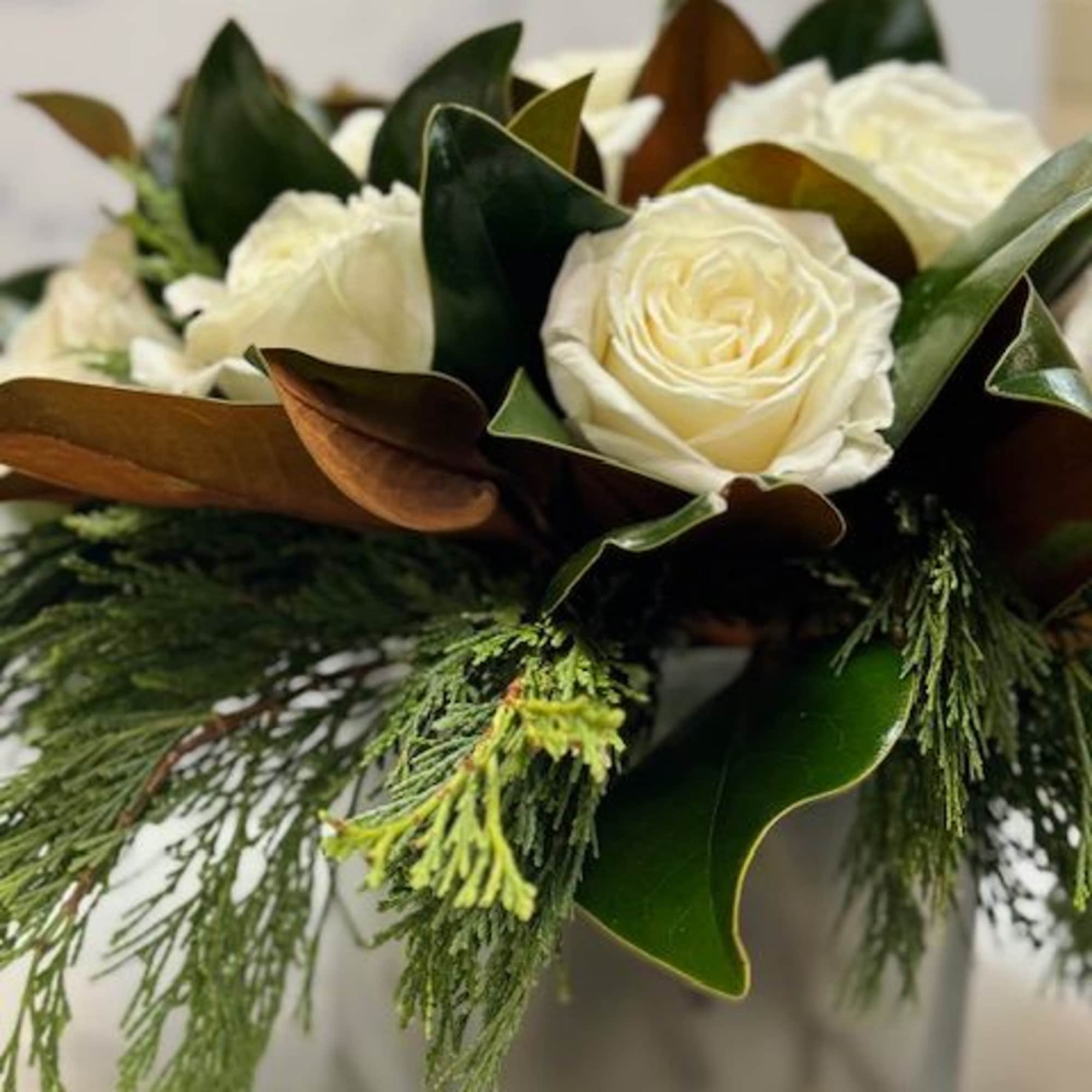 Arrangement filled with winter greens, magnolia, and white roses