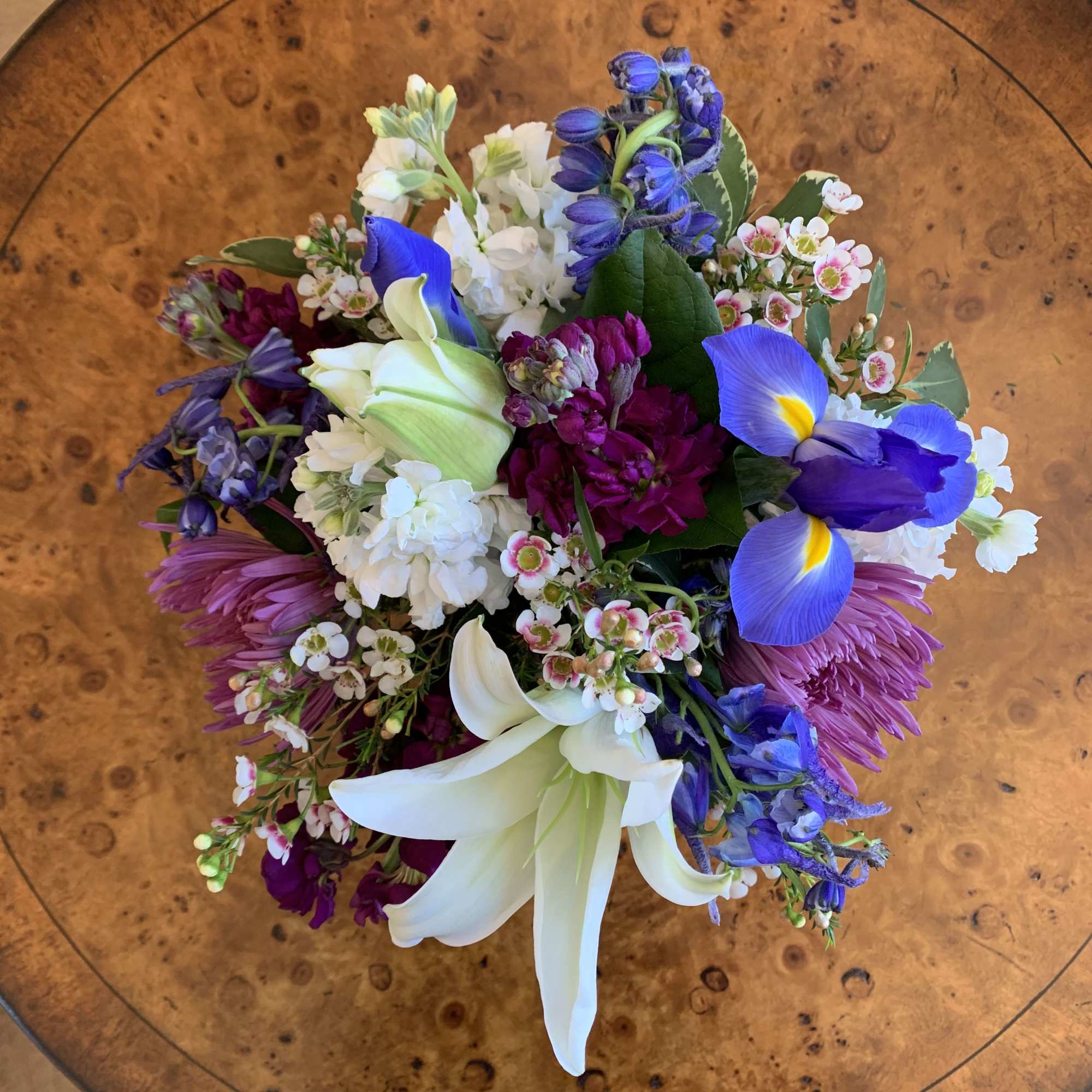 White lily, iris, white and purple stock, blue delphinium, lavender spidermums arranged