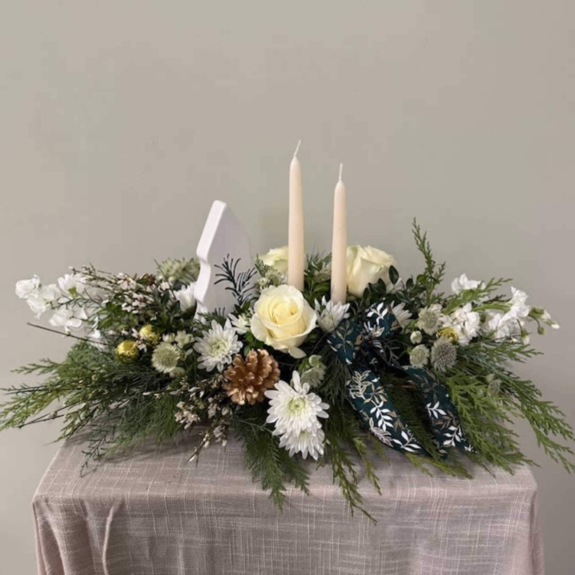 Double candle centerpiece includes winter greens, florals and a ceramic keepsake Christmas