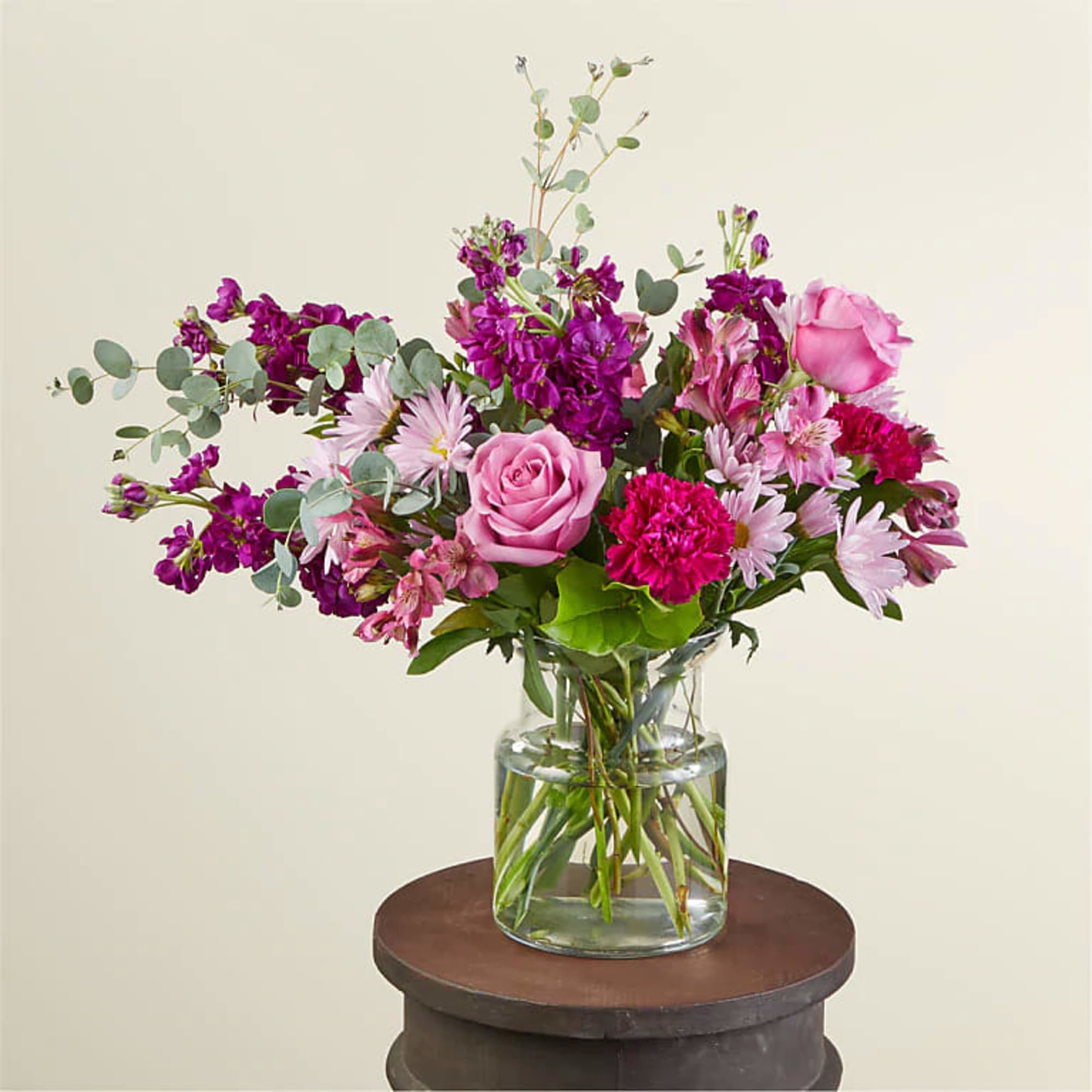 This arrangement features berry hues of carnations, daisies, roses, stock, and greens.