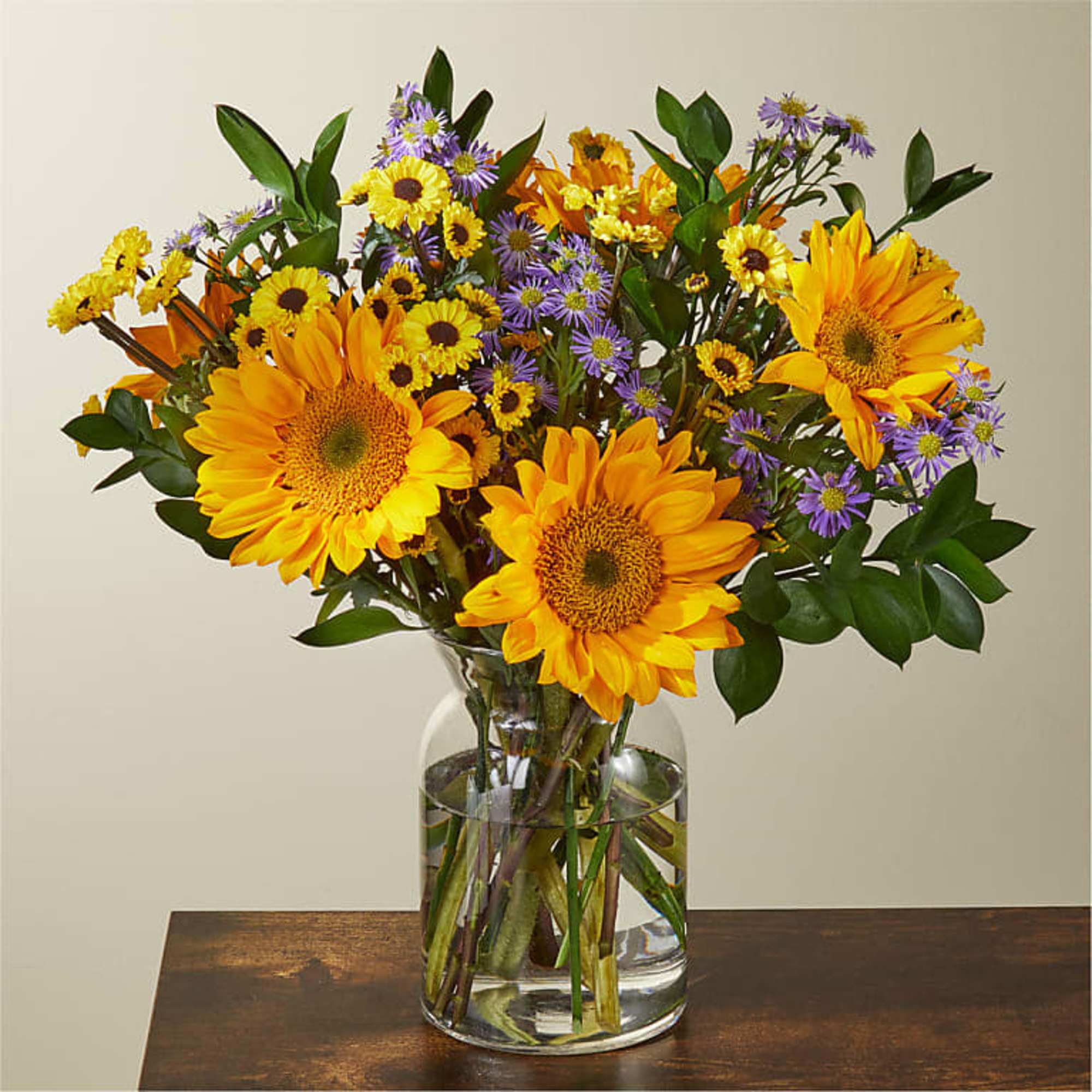 This arrangement features a gold burst of sunflowers, spring poms, and green