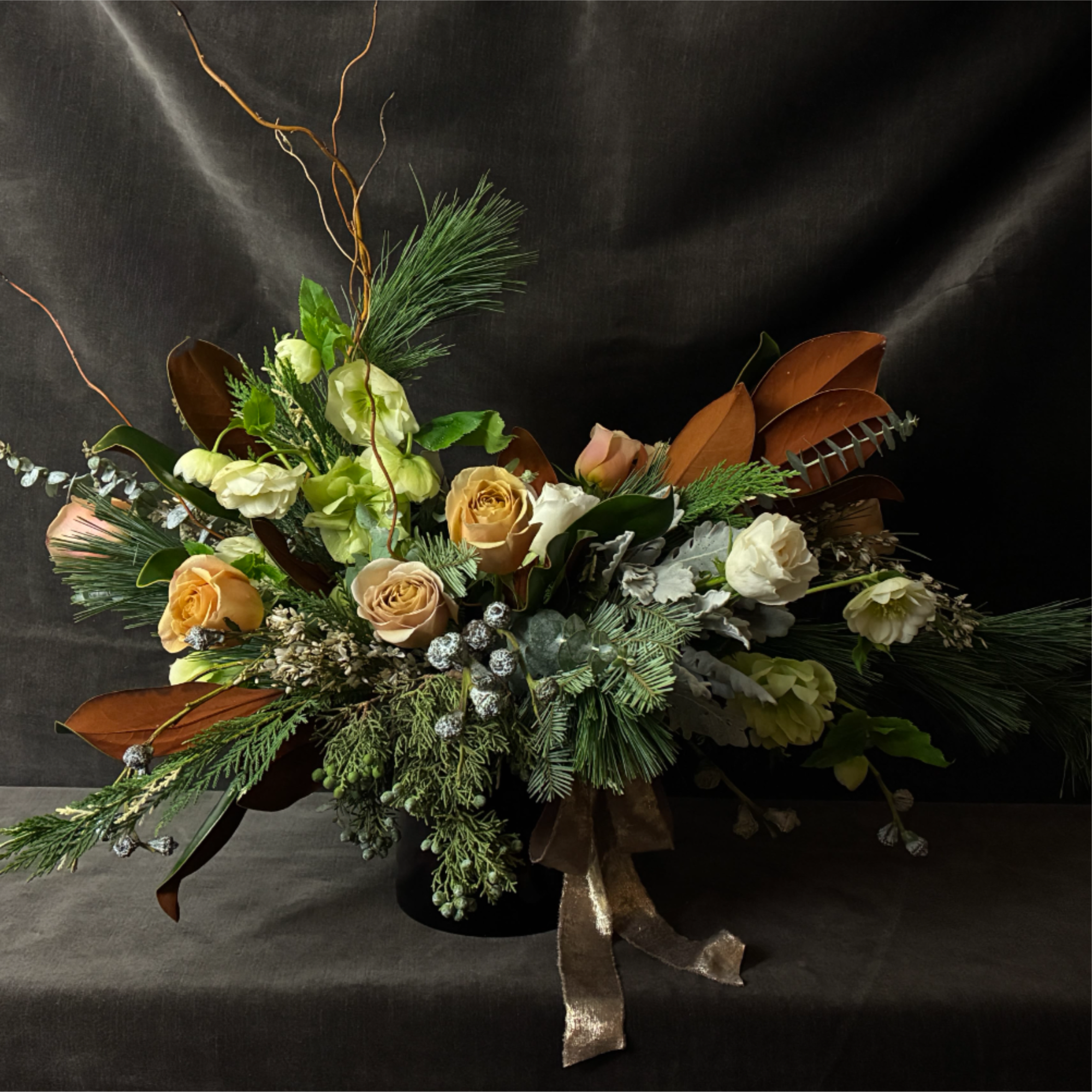 The Golden Hearth Arrangement is a luxurious mix of garden roses, wintergreens