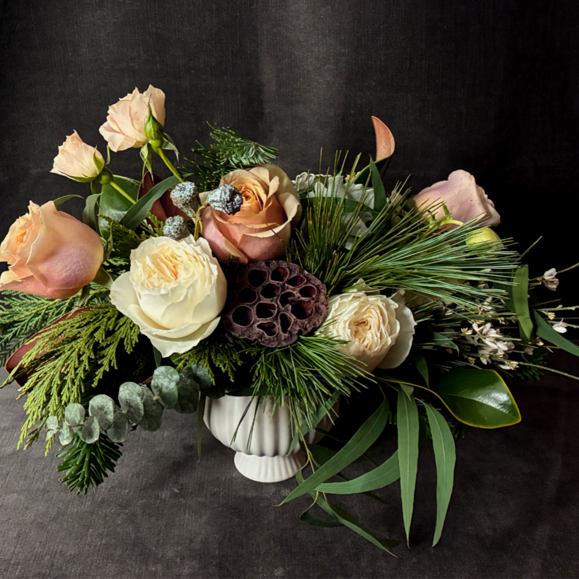 The Golden Hearth Arrangement is a luxurious mix of garden roses, wintergreens