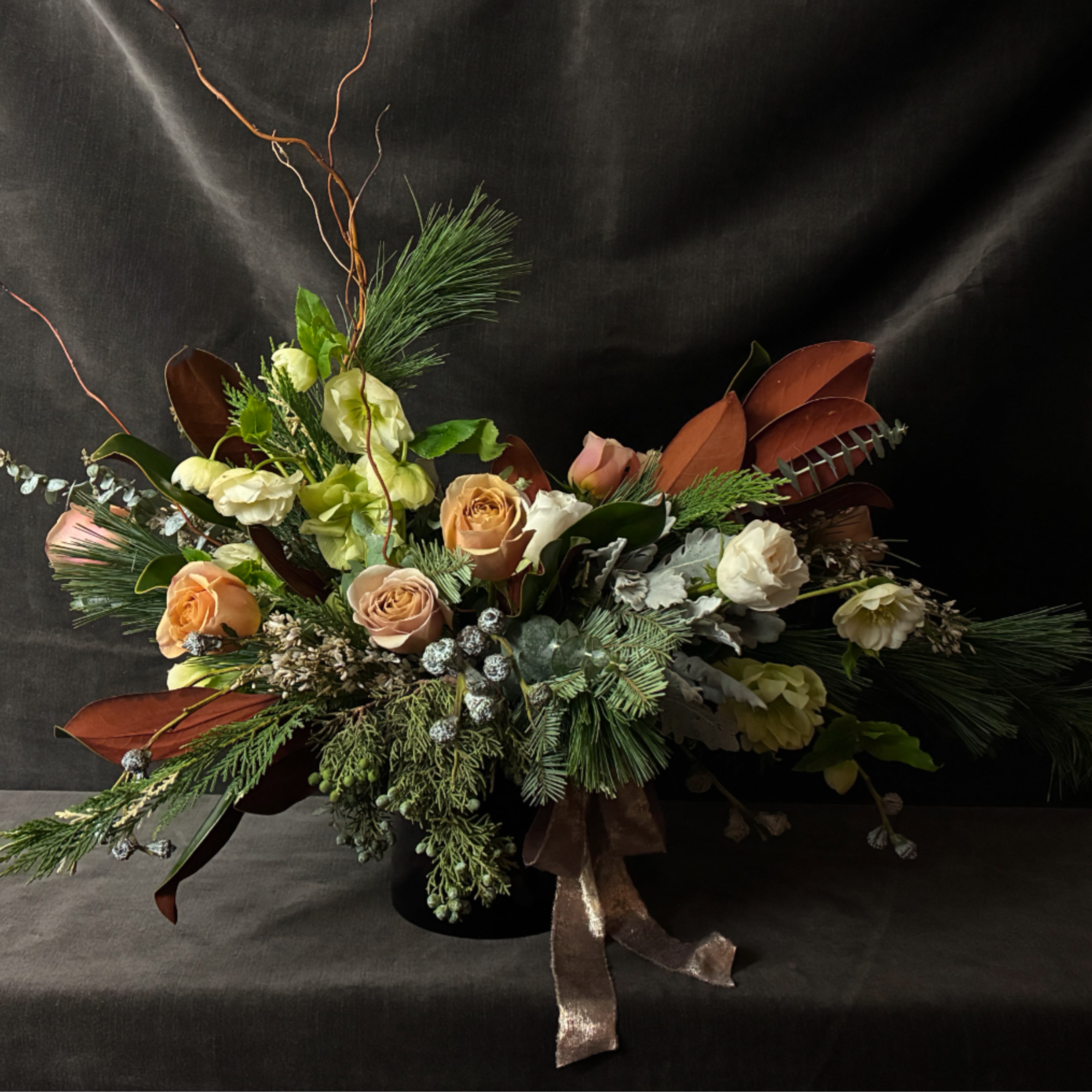 The Golden Hearth Arrangement is a luxurious mix of garden roses, wintergreens