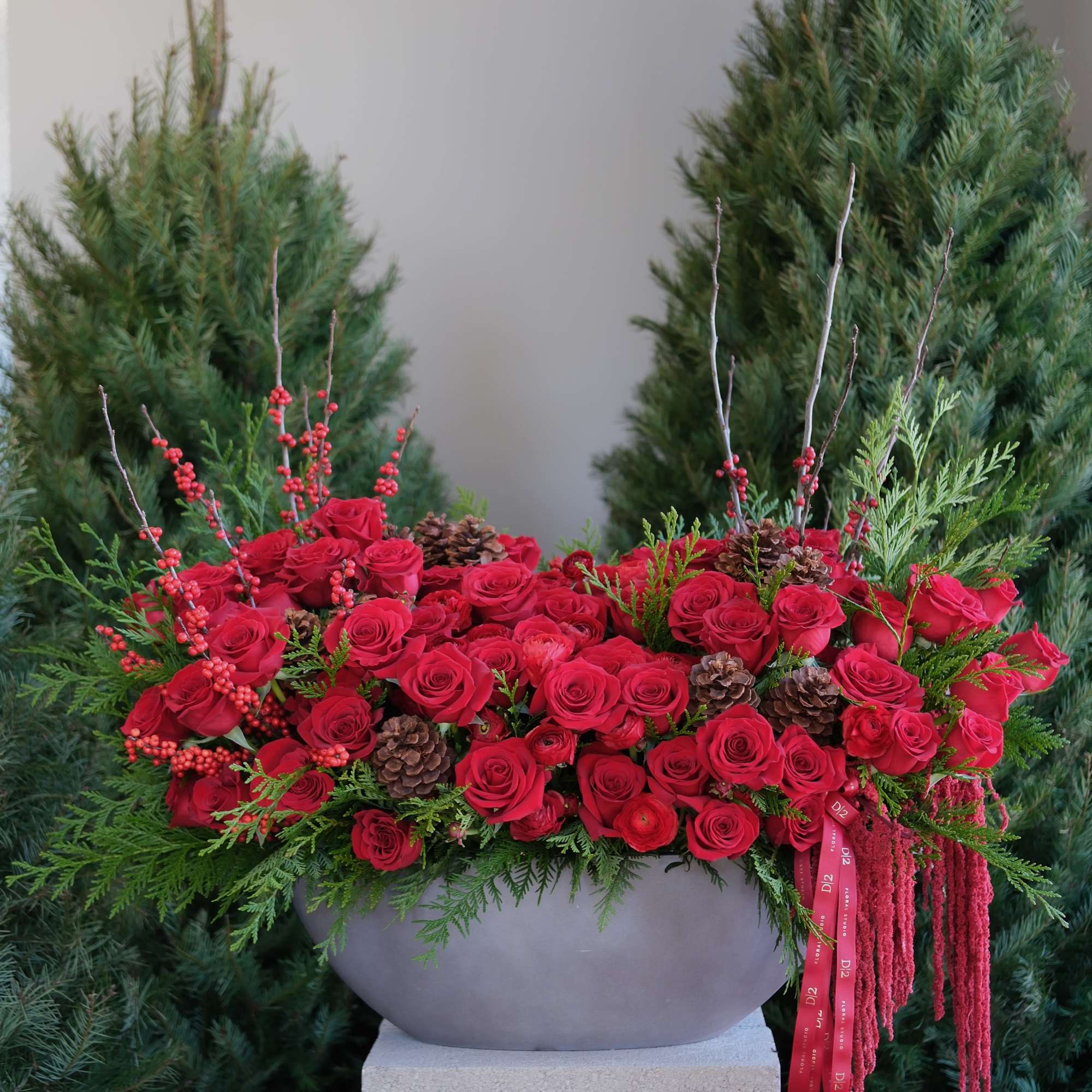 A lush display of red roses, evergreens, pinecones, and berries arranged in